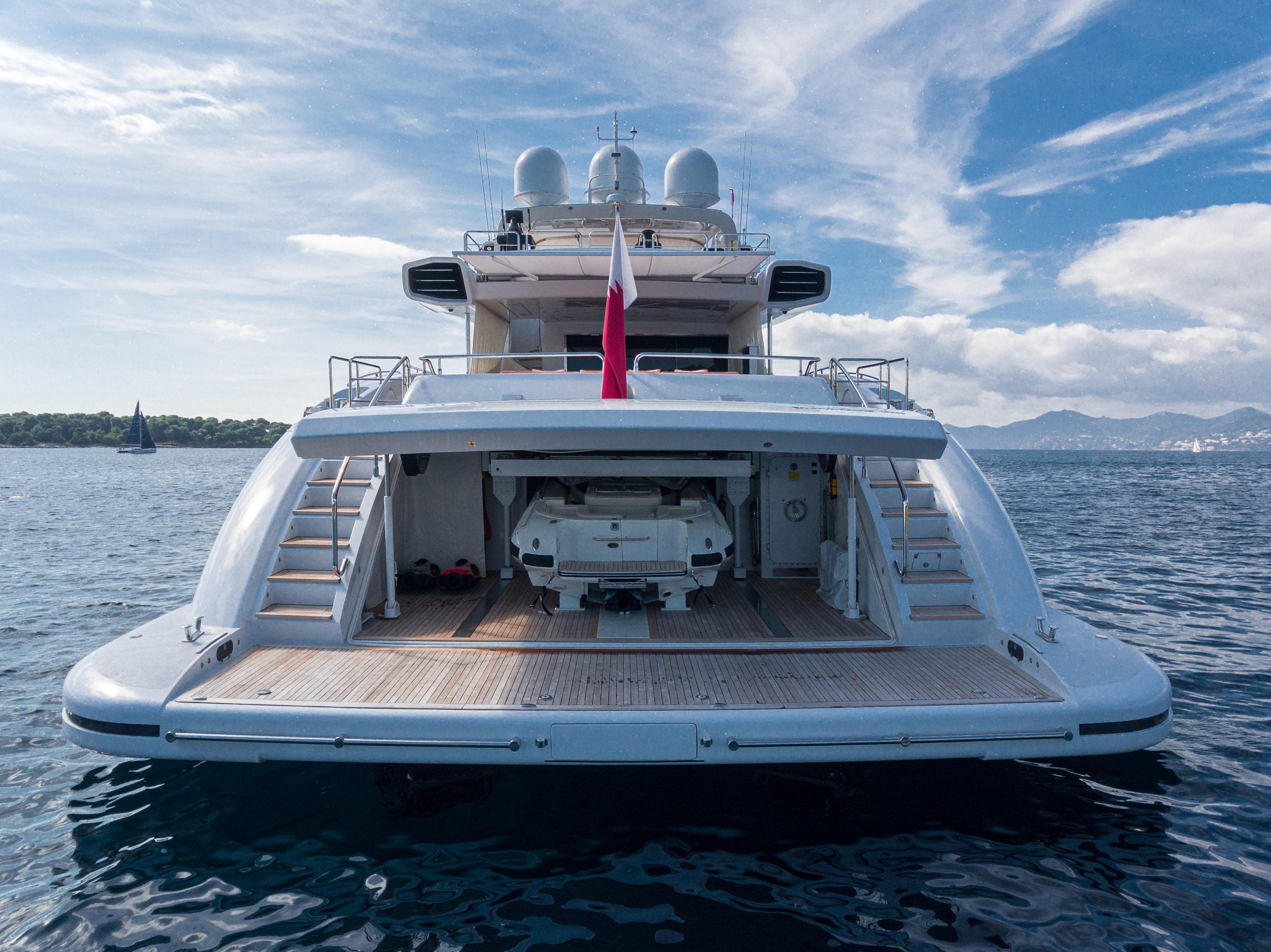 Luxury 2011 Mangusta 165 yacht with open garage, docked on serene waters under a blue sky.