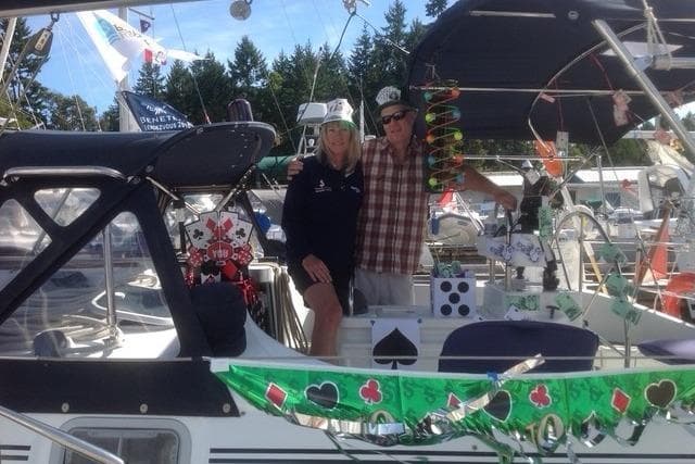 Couple on decorated 1995 Beneteau Oceanis 400 sailboat, festive atmosphere, docked in marina.