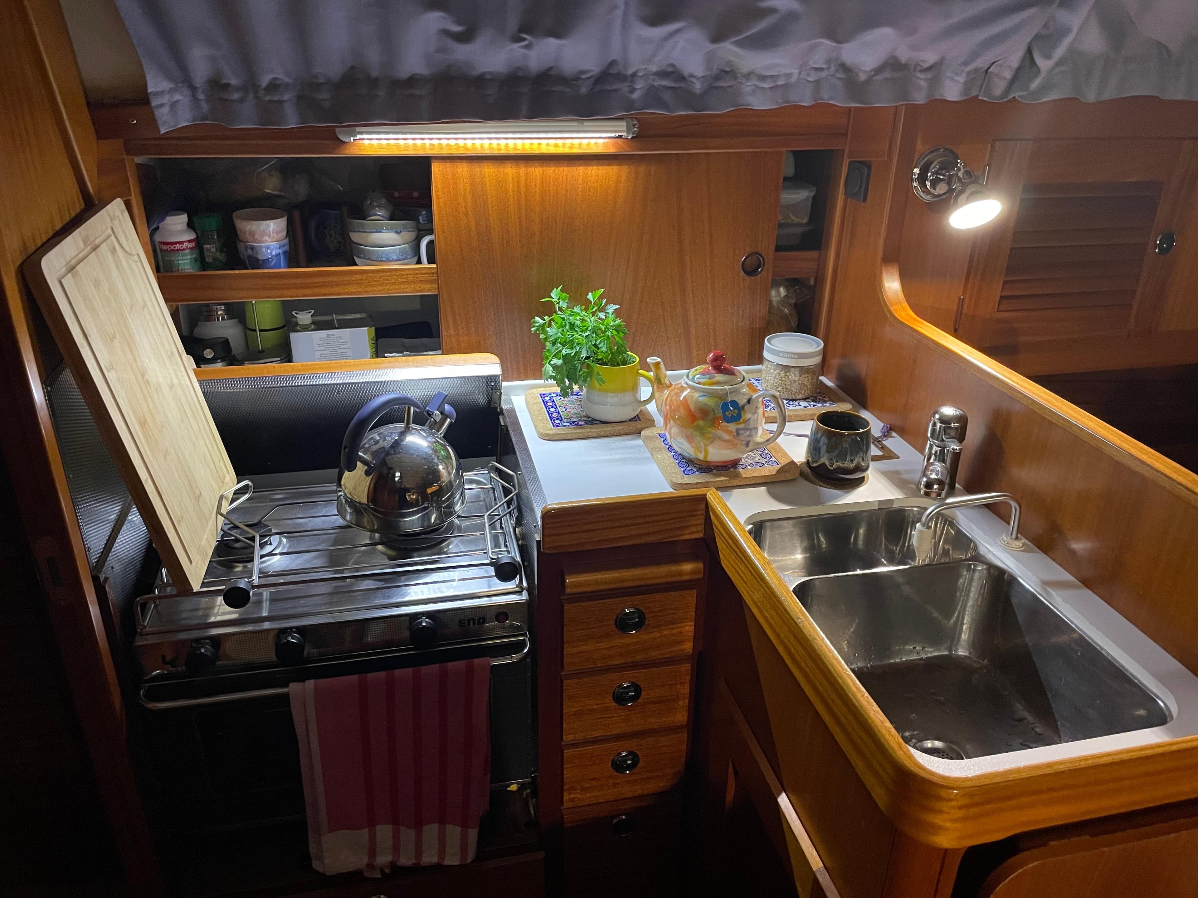 Cozy kitchen area in a 2003 Hallberg-Rassy 34 sailboat with stove, sink, and wooden cabinetry.