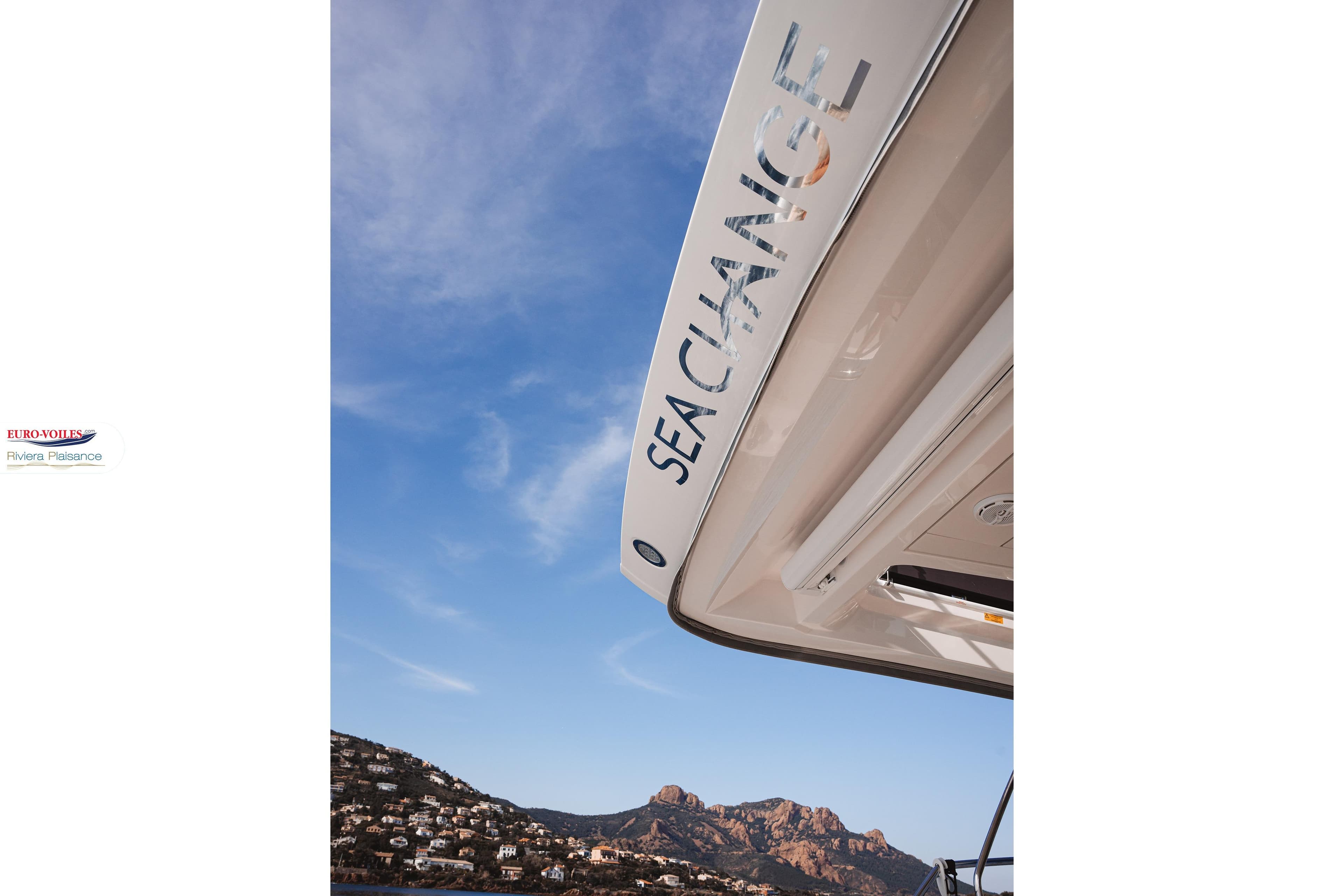 Prestige 590 Fly yacht with "Sea Change" text, 2021 model, against a scenic coastal backdrop.
