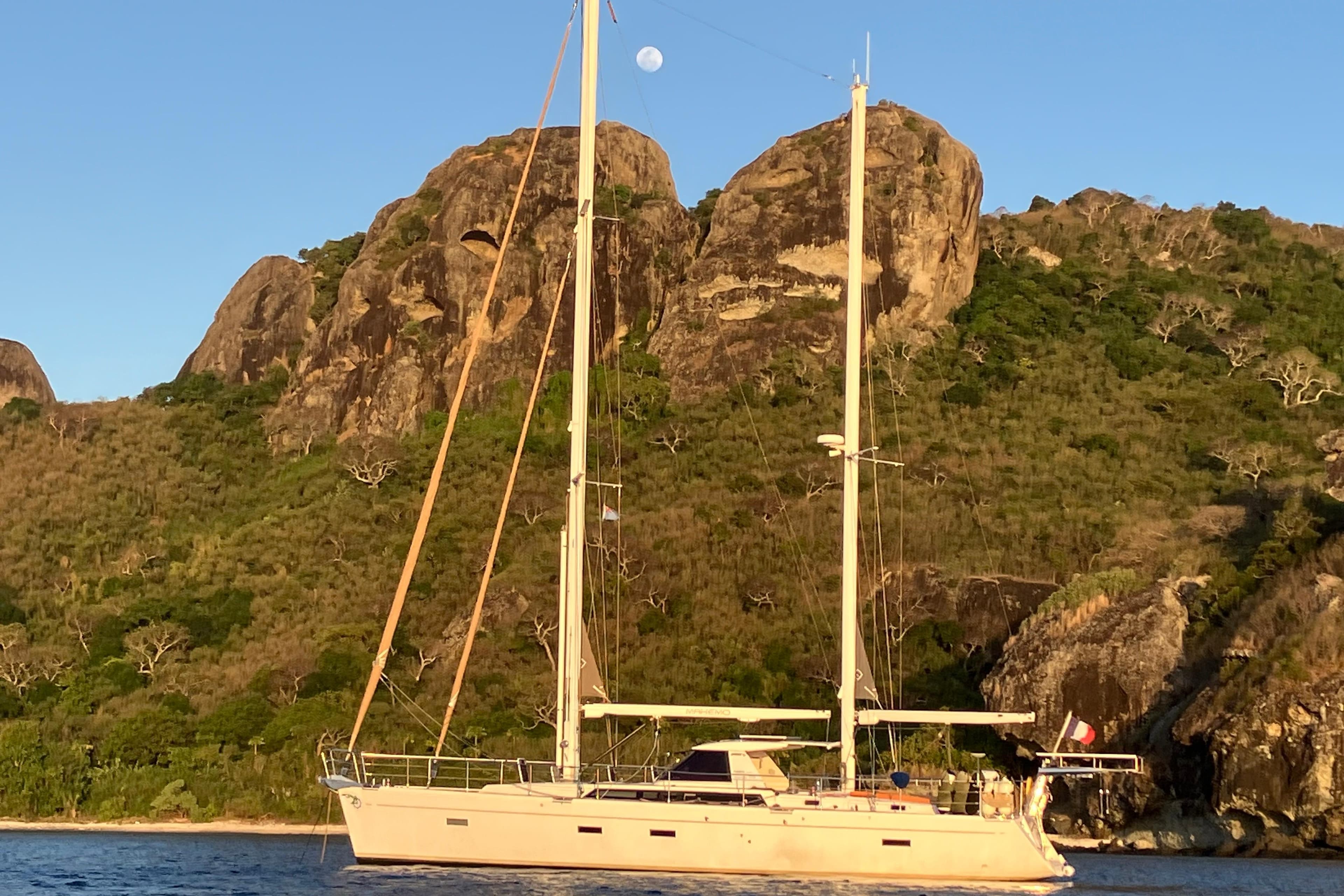 Sailing yacht Amel 55 (2011) anchored near rocky coastline under a clear sky.