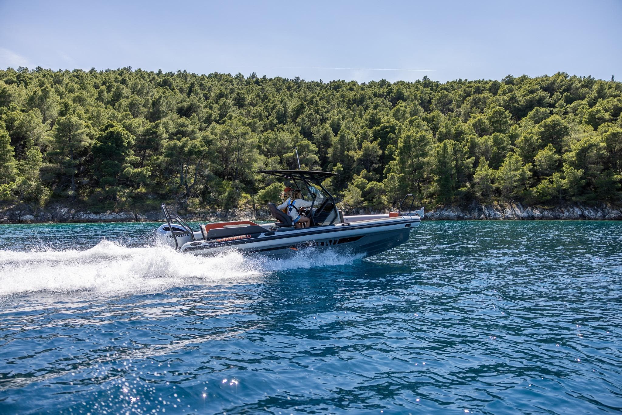 2026 Highfield ADV7 boat cruising on clear blue water near a lush green forest.