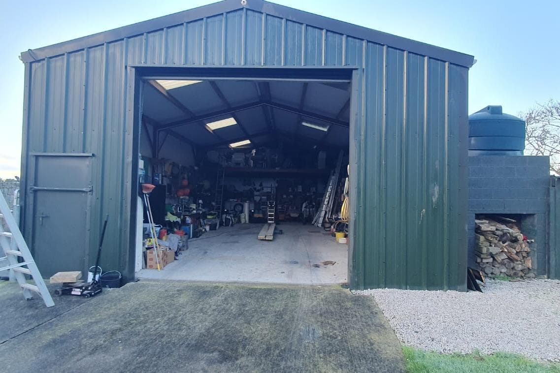 Open green metal garage with tools and equipment inside, featuring a 1989 Fairey Spearfish MKIII.