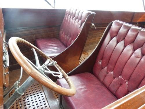 Interior of a 1924 Morris 30 Commuter Launch with vintage leather seats and wooden steering wheel.
