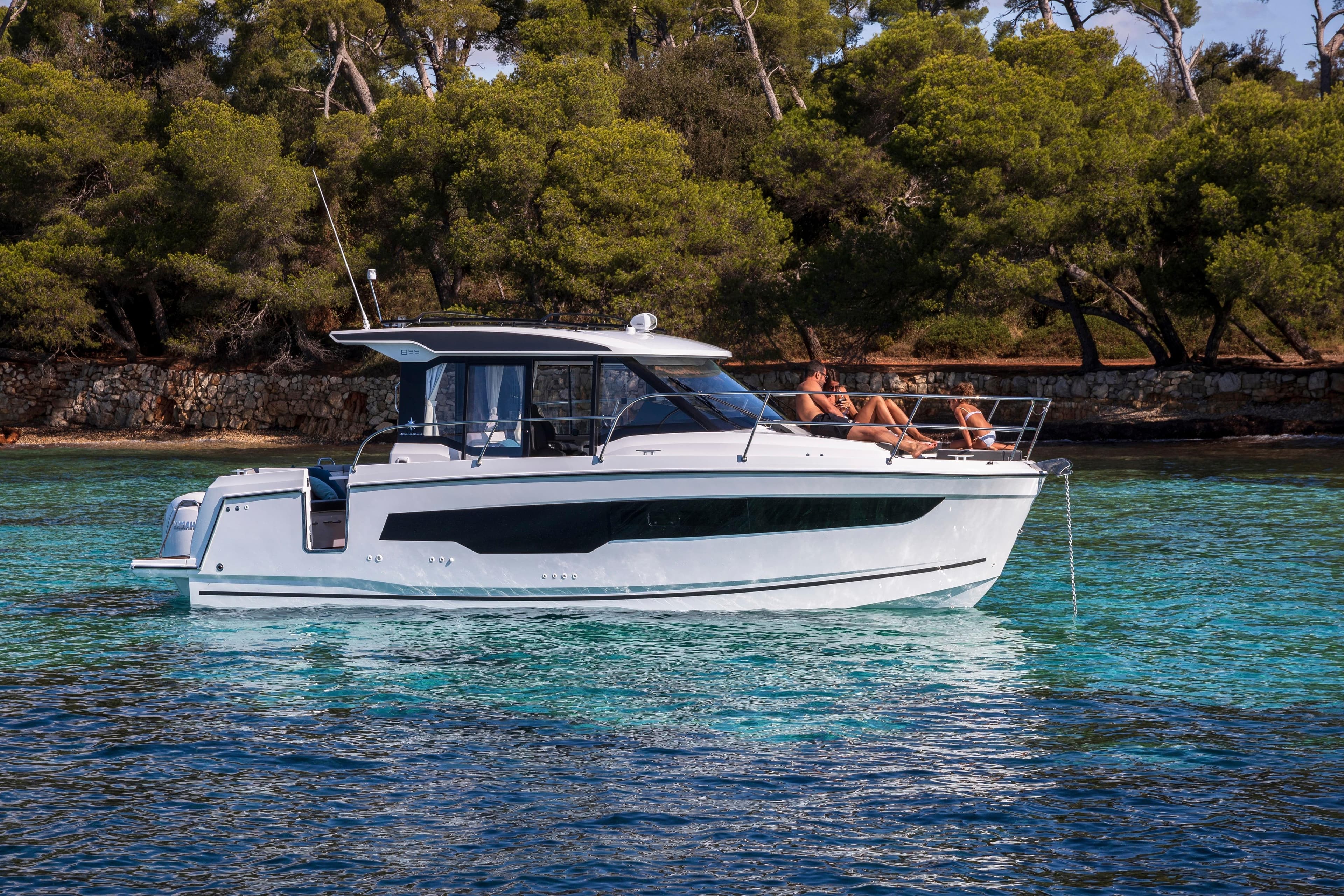 2026 Jeanneau NC 895 Series 2 boat cruising on clear turquoise water near a forested shoreline.