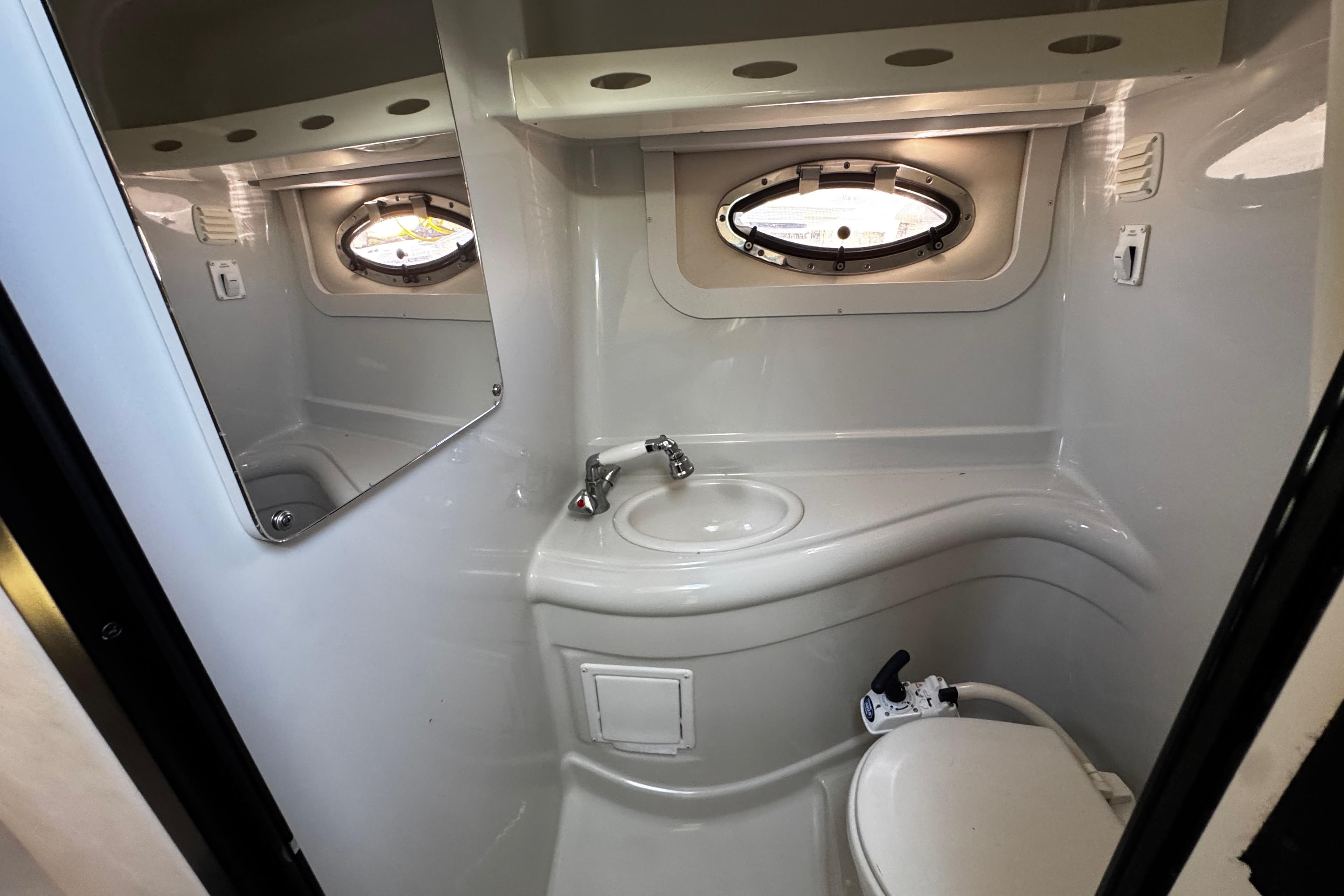 2004 Crownline 250 CR boat bathroom with sink, mirror, and porthole window.
