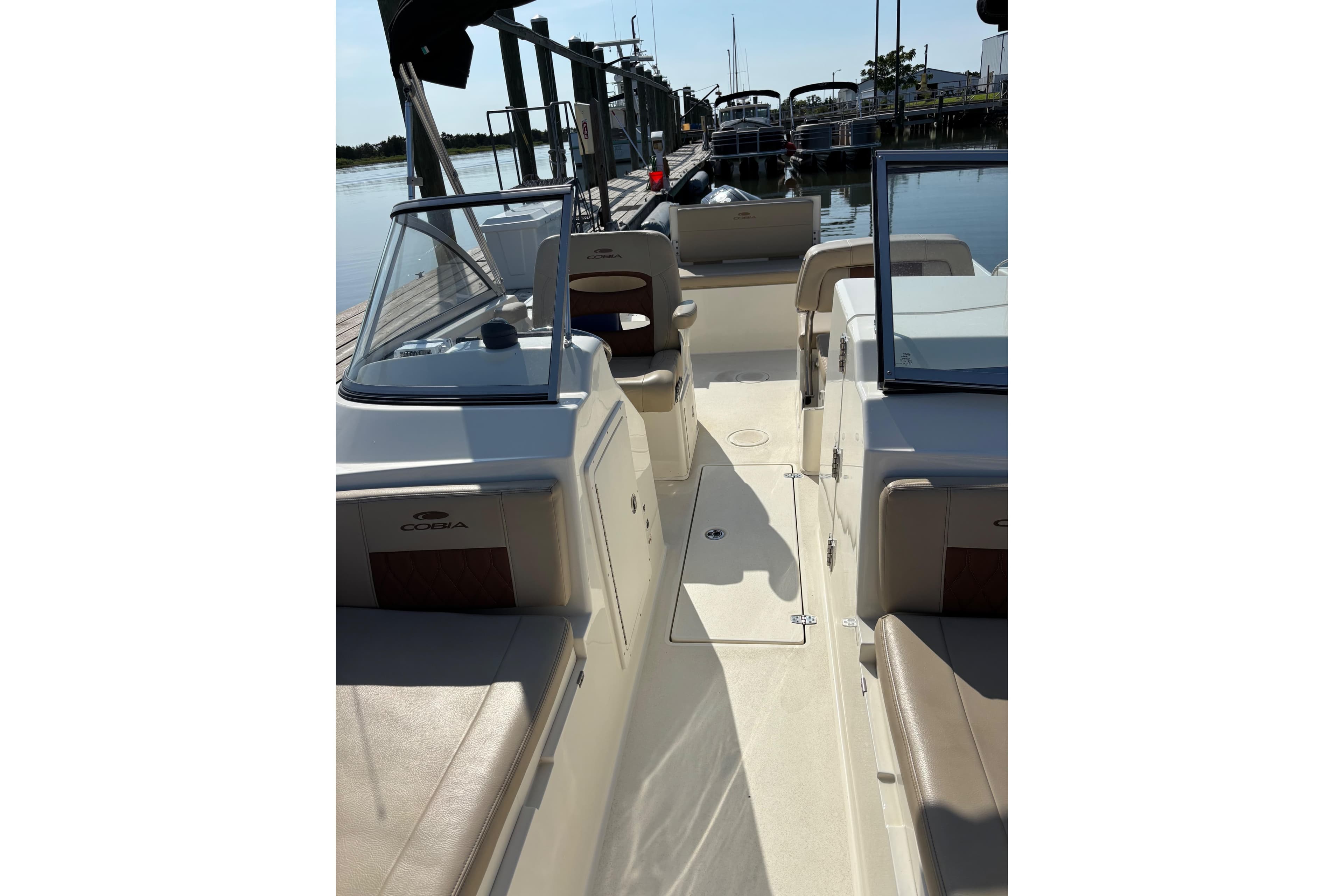 2024 Cobia 220 Dual Console boat interior with seating and windshield, docked by the water.