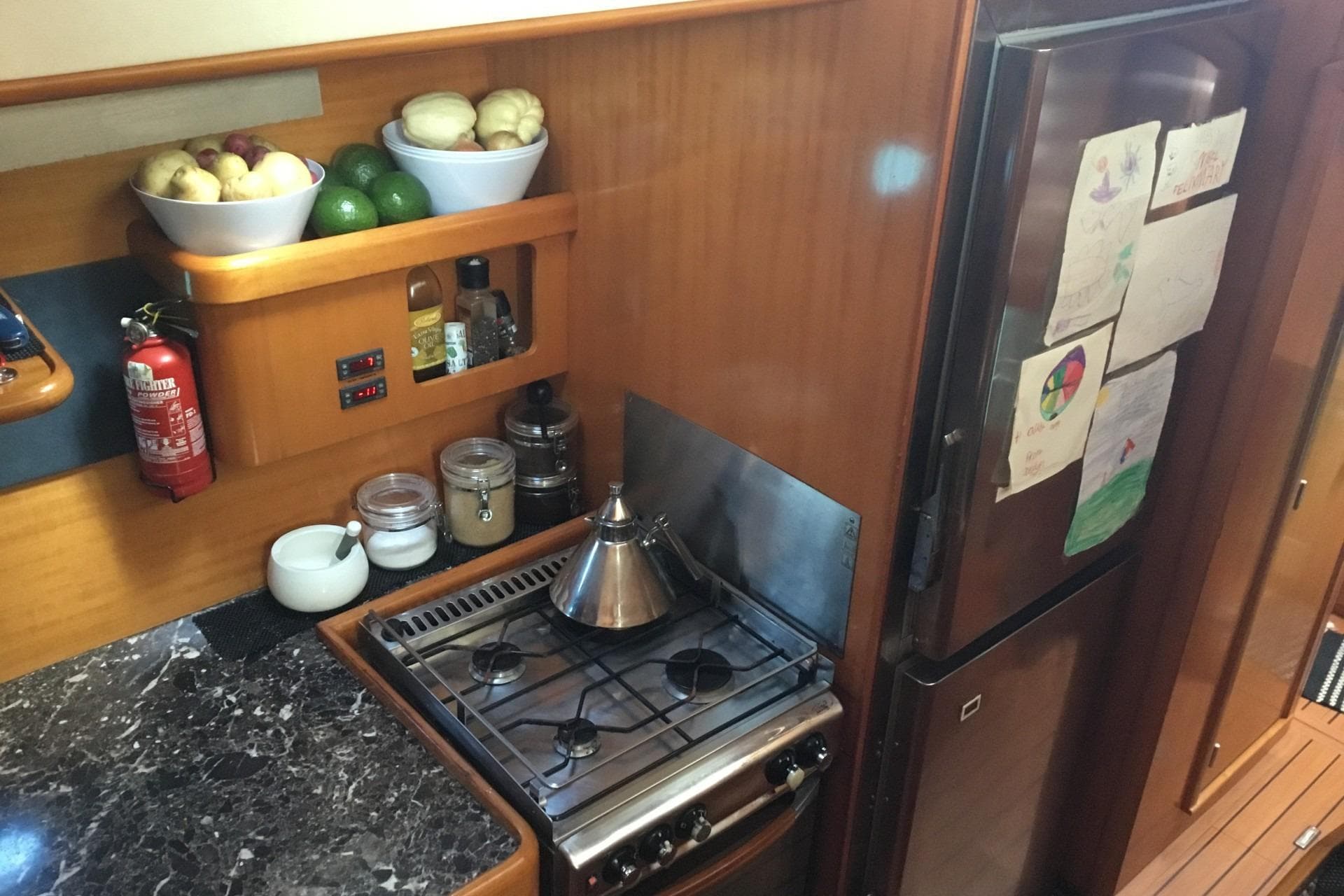 Cozy kitchen in 2002 Lagoon 470 yacht with stove, fridge, and fruit bowls.