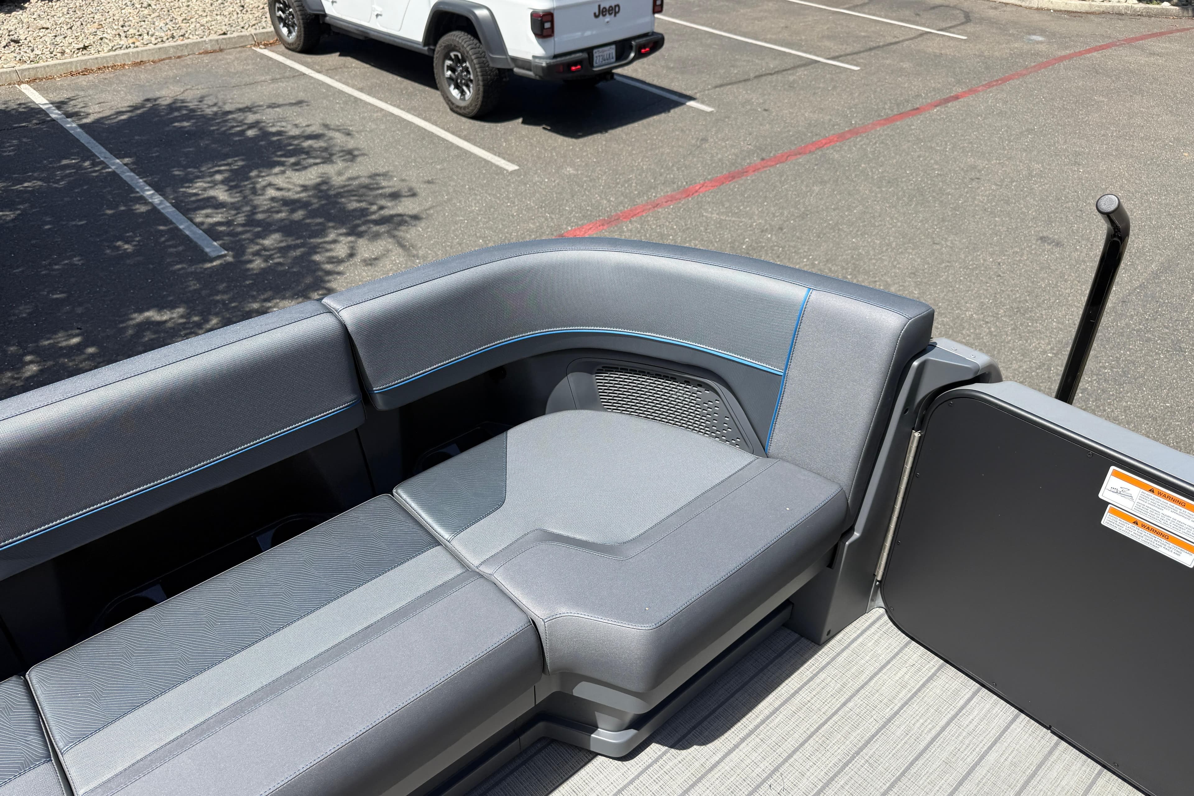Luxurious seating on 2025 Manitou Explore Dual Engine pontoon boat in a parking lot.