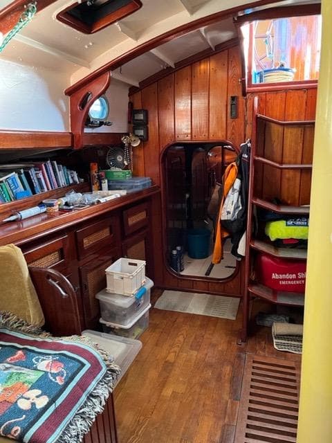 Cozy wooden interior of 1985 Thomas Colvin "Pipistrelle" sailboat with books and storage.