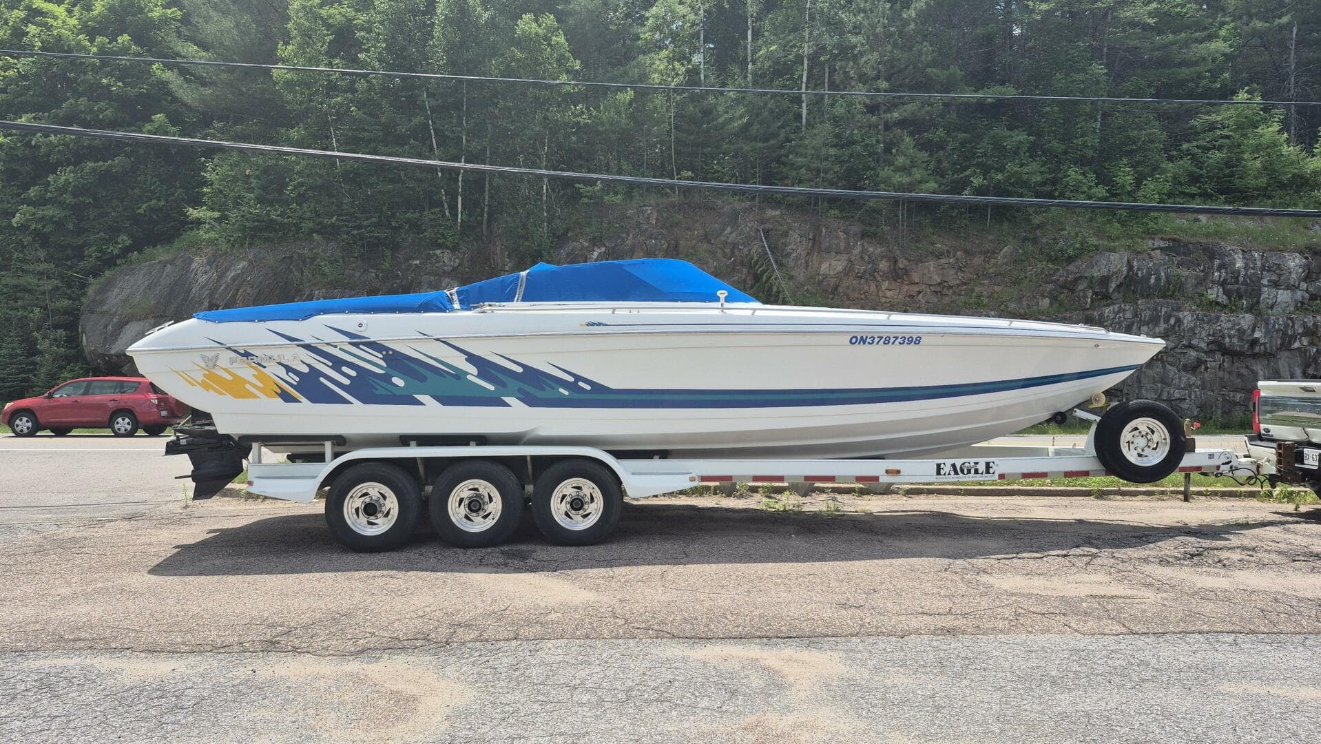 1999 Formula Fastech boat on trailer, vibrant graphics, parked outdoors with forest background.