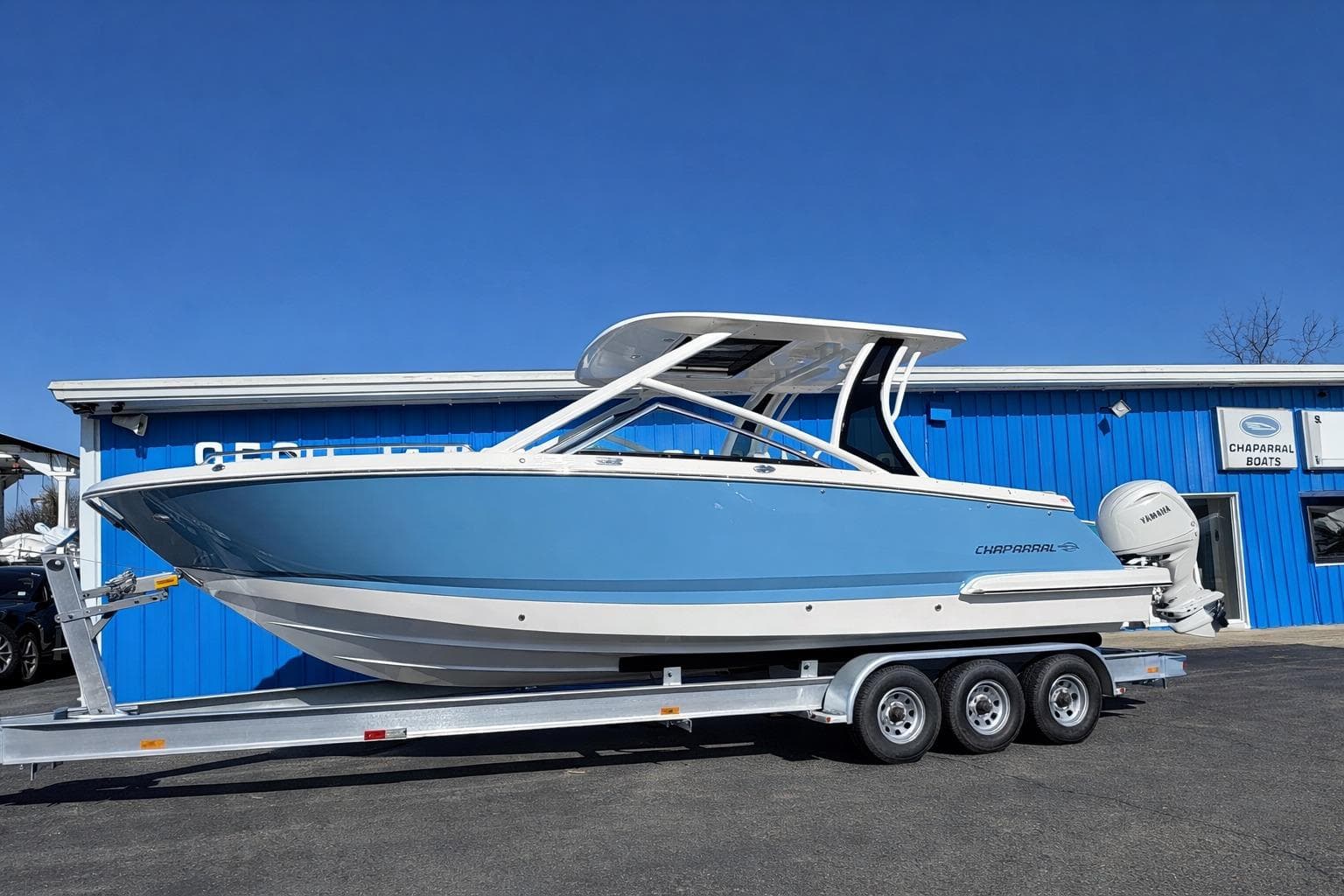 2026 Chaparral 280 OSX boat on trailer, parked outside blue building under clear sky.