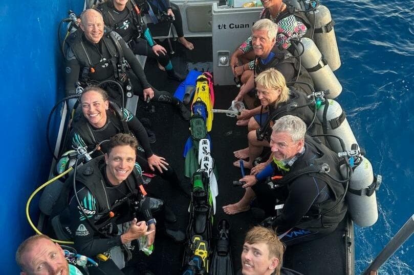 Group of divers on a 1987 custom trimaran, preparing for a dive in clear blue waters.