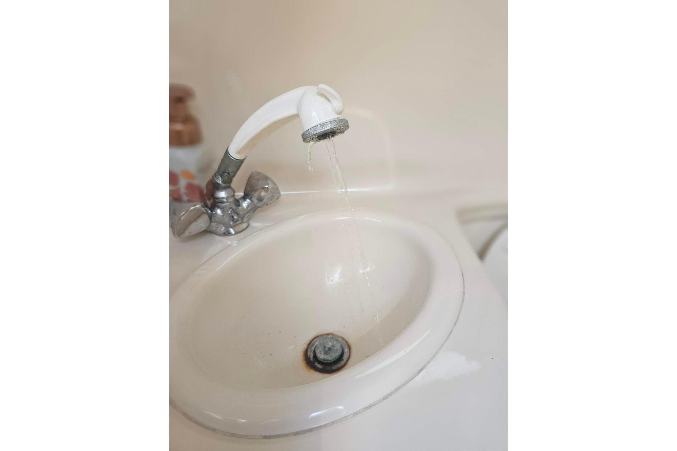 A white sink with a running faucet, indoors, close-up view.