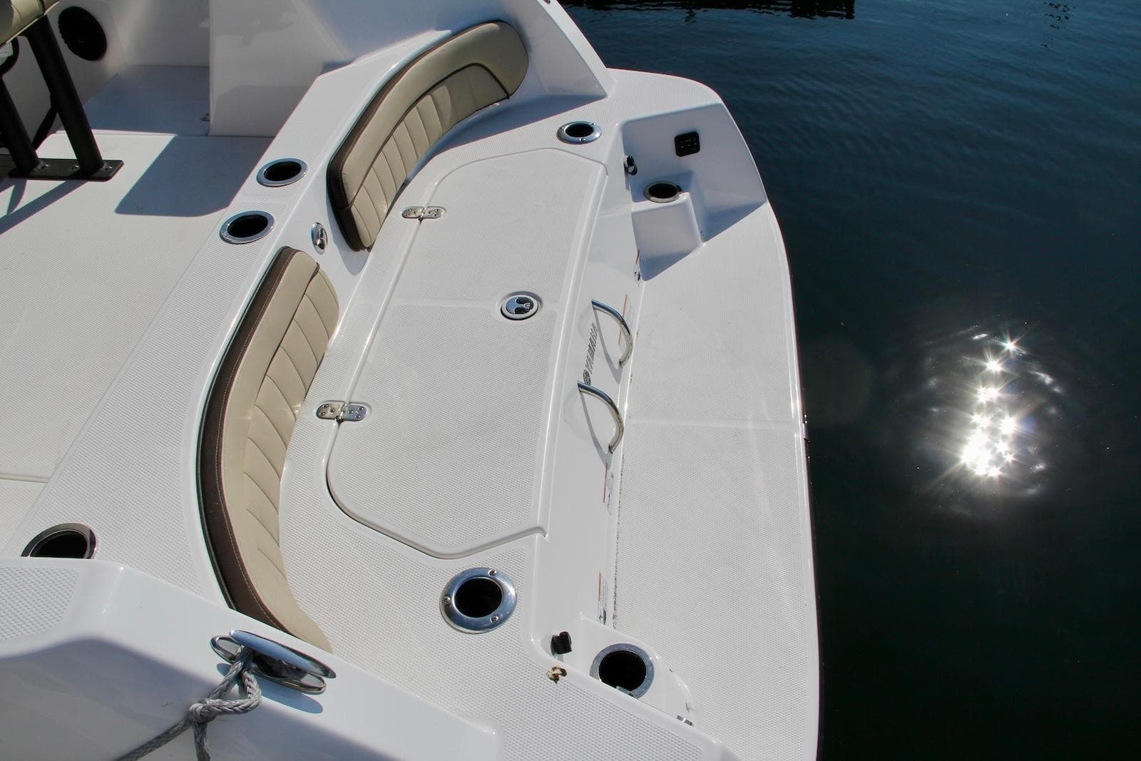 2024 Yamaha Boats 222 FSH Sport E deck with seating and cup holders, reflecting sunlight on water.