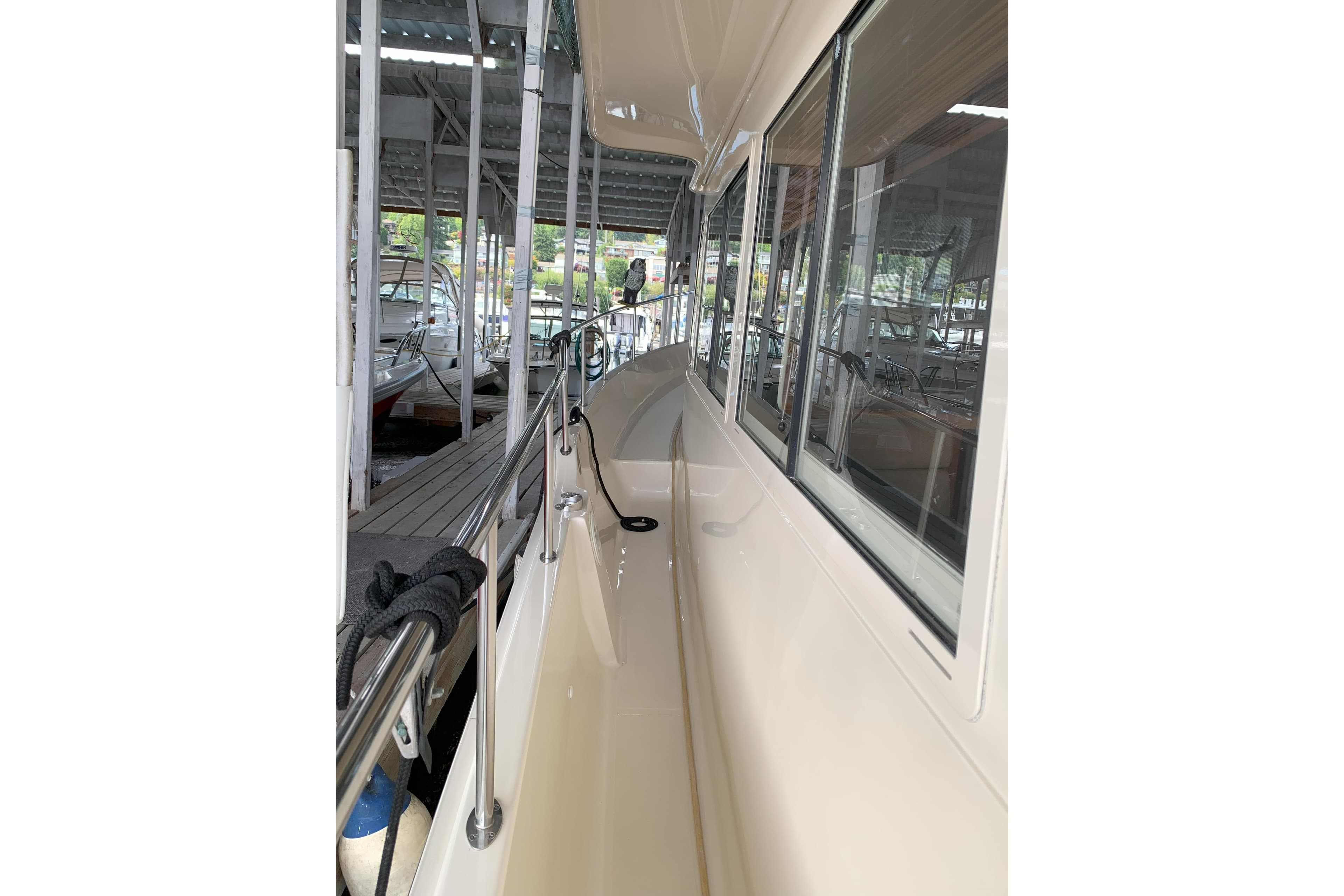 2007 Mainship 34 Trawler side deck view in marina, showcasing sleek design and railing.