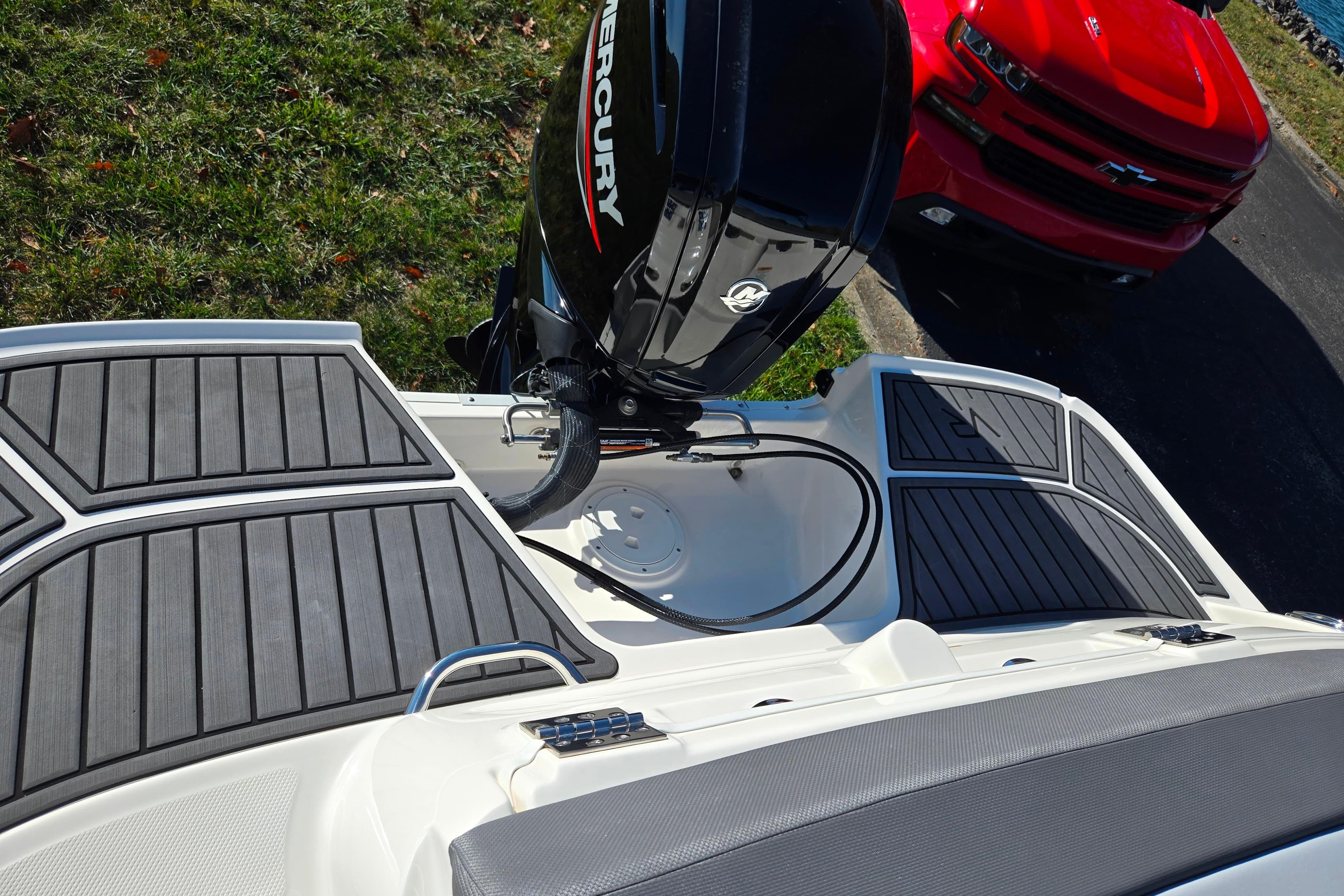 2024 Bayliner VR5 Bowrider OB with Mercury outboard engine, parked near a red vehicle.
