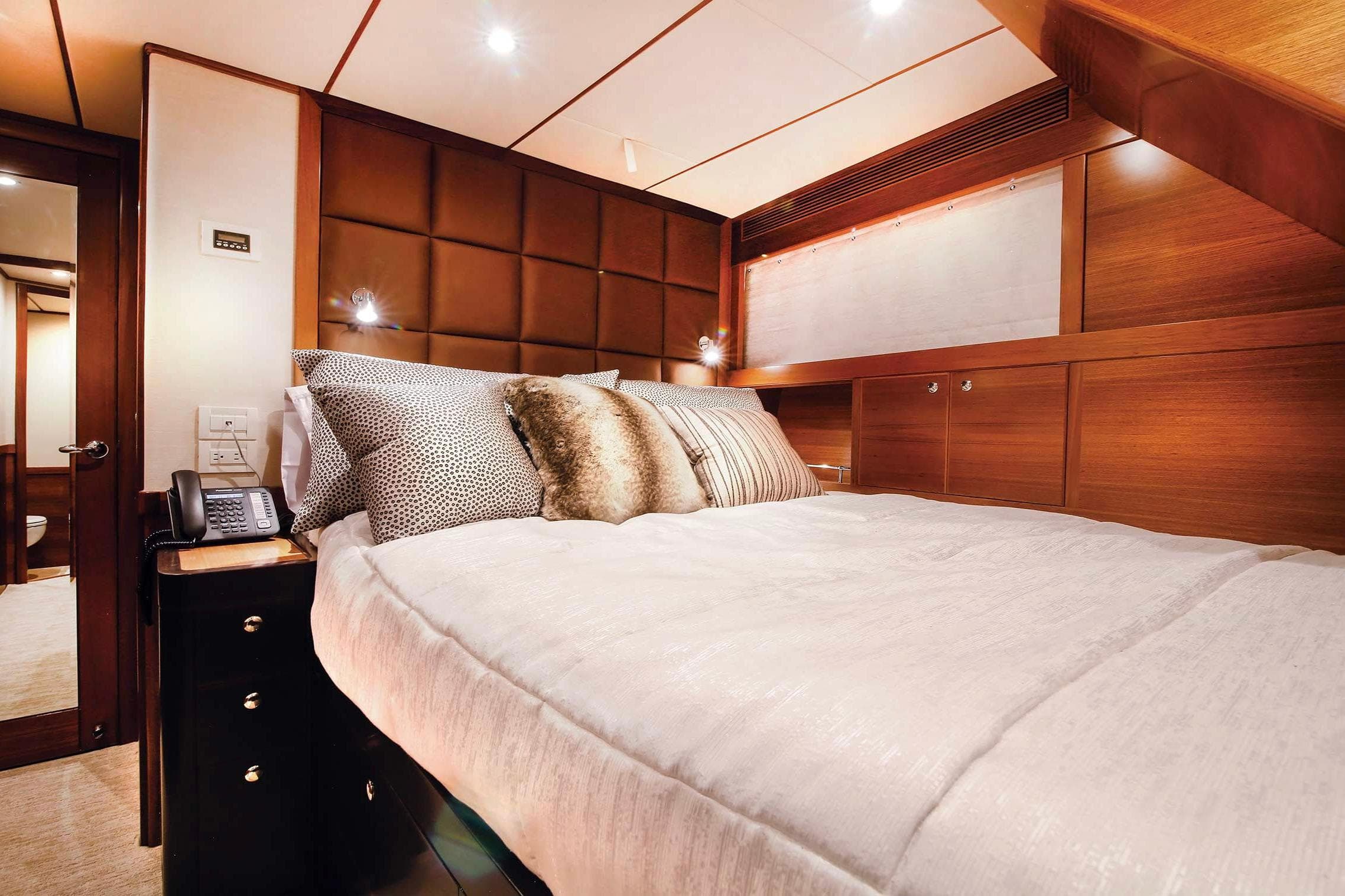 Luxurious bedroom interior of 2018 Nordhavn 76 yacht with plush bedding and wood paneling.