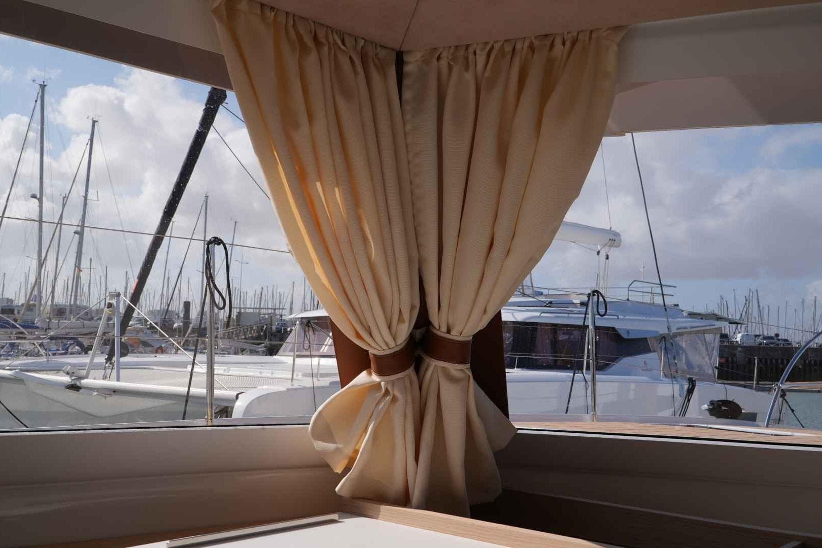 Interior view from a 2026 Fountaine Pajot Tanna 47 yacht, overlooking marina with sailboats.