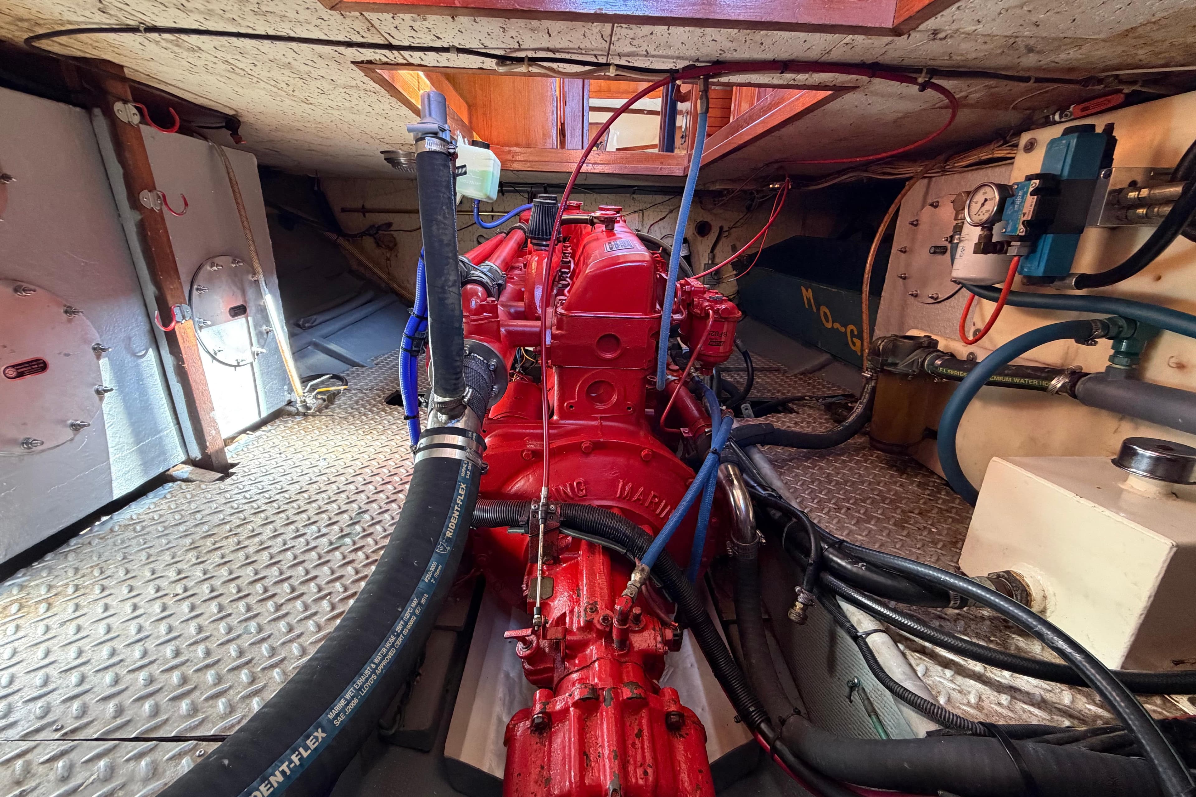 Engine room of 1982 Lien Hwa 31 boat, featuring a red marine engine and various hoses.