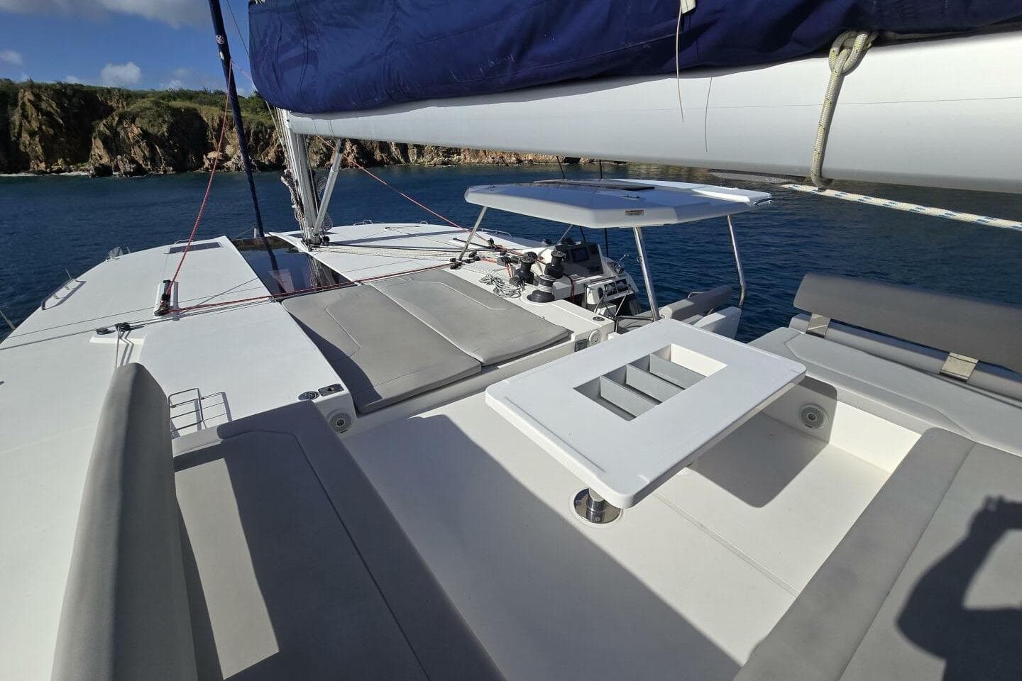 Leopard 50 catamaran deck with seating and table, 2020 model, anchored near rocky coastline.