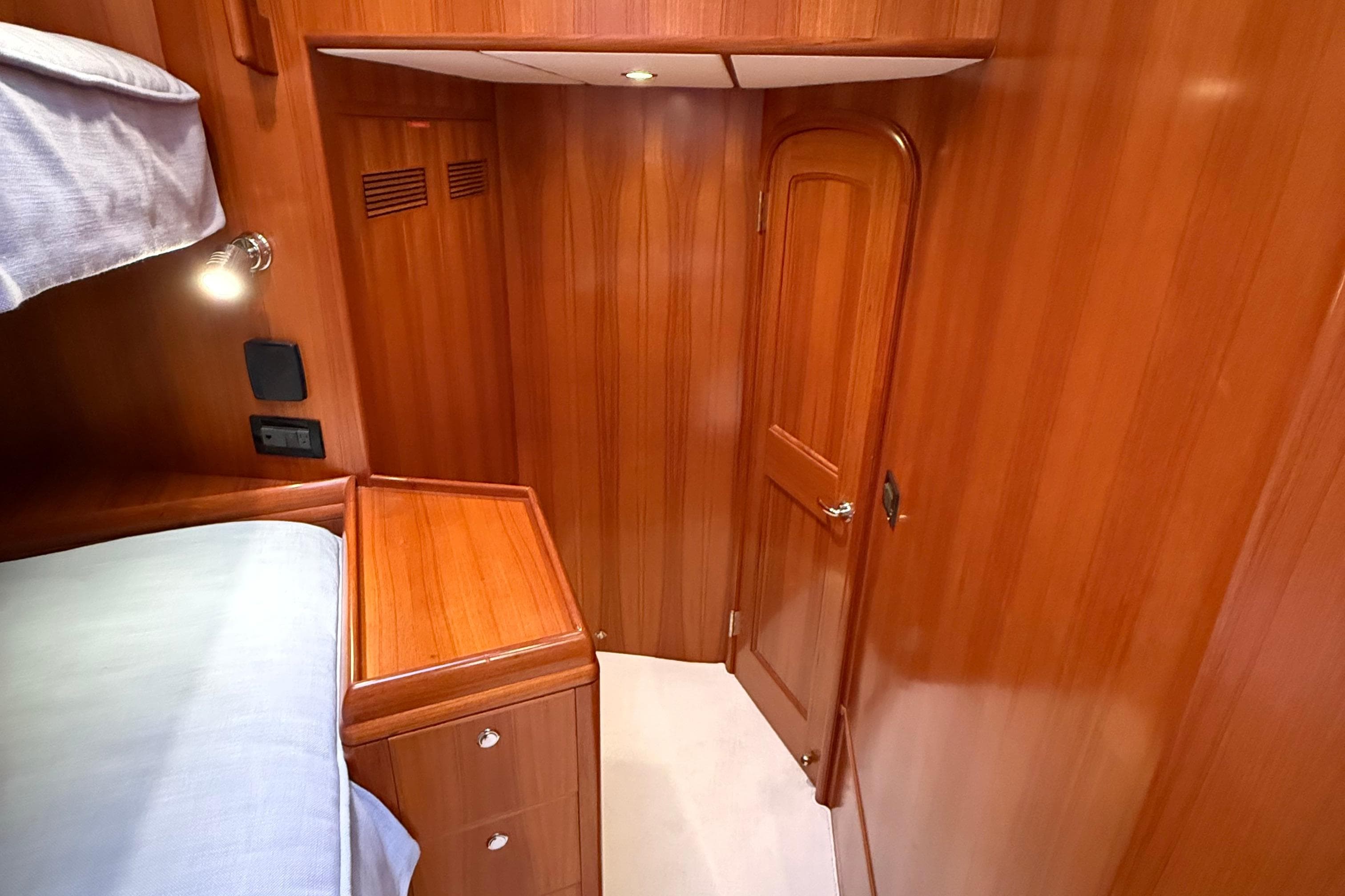 Luxurious wooden interior of 2009 Nordhavn N64 yacht cabin with bed and door.