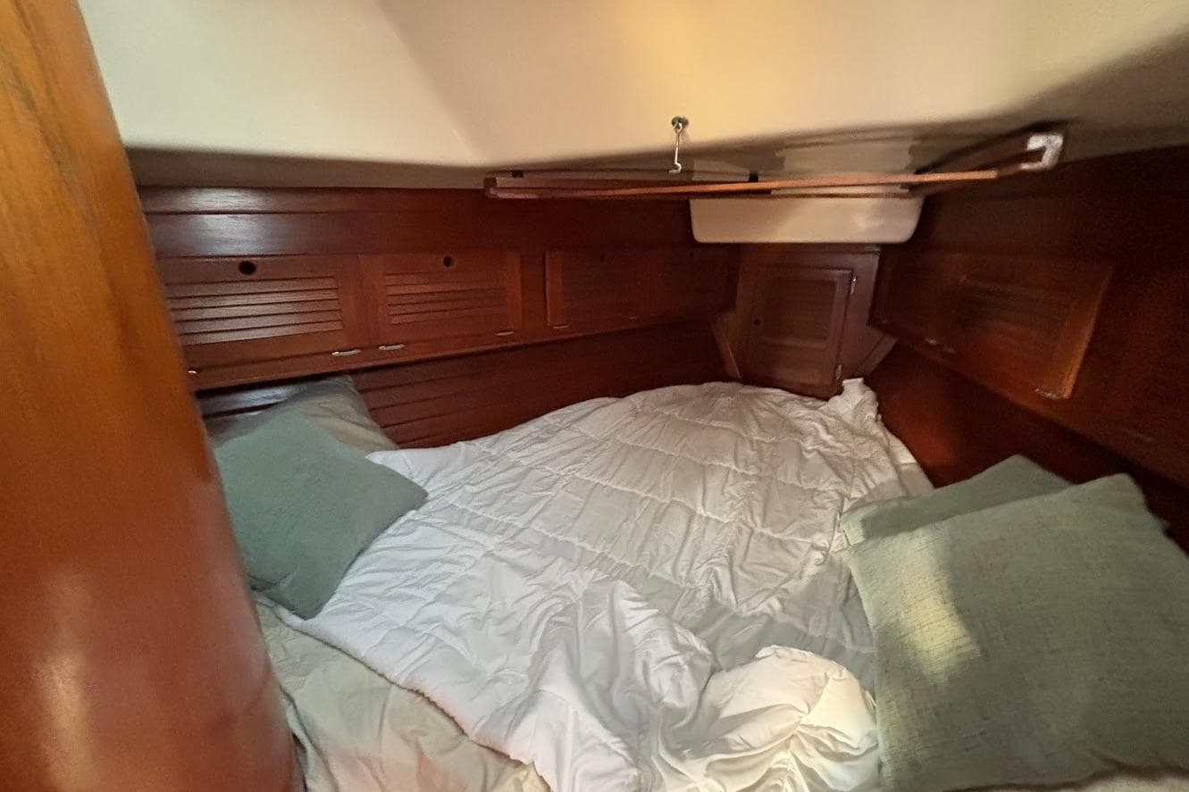 Cozy cabin interior of 1983 Bristol 38.8 sailboat with wooden finish and bedding.