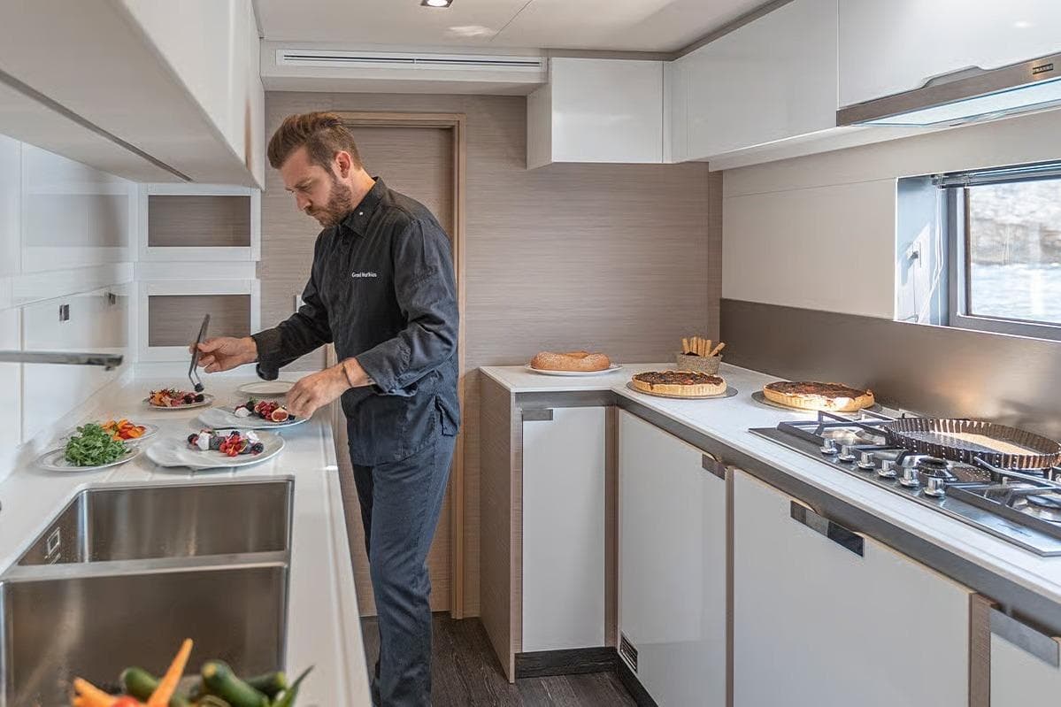 Chef preparing dishes in the modern kitchen of a 2026 Fountaine Pajot Samana 59 yacht.