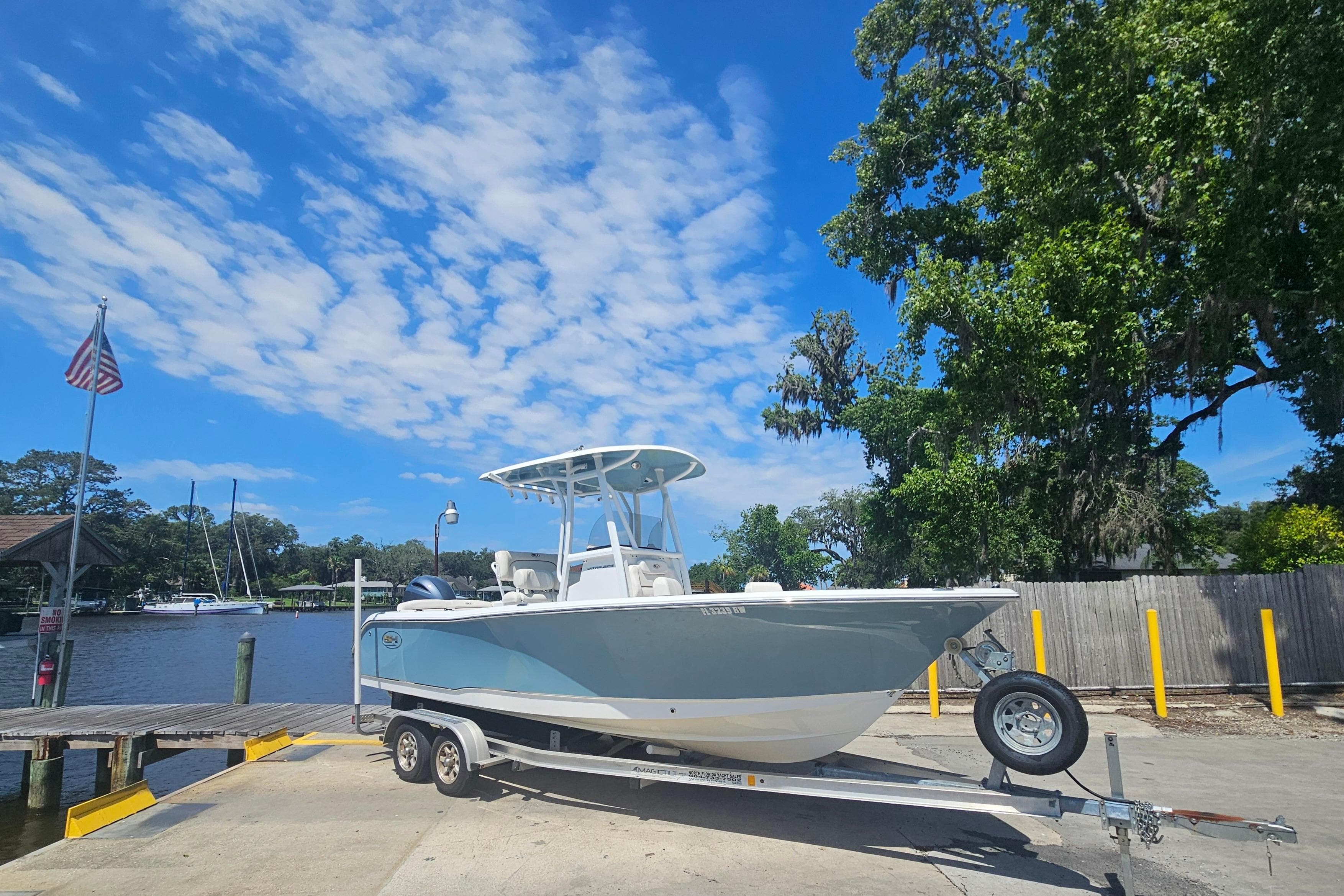 2019 Sea Hunt Ultra 225 boat on trailer at a scenic dock under blue sky.