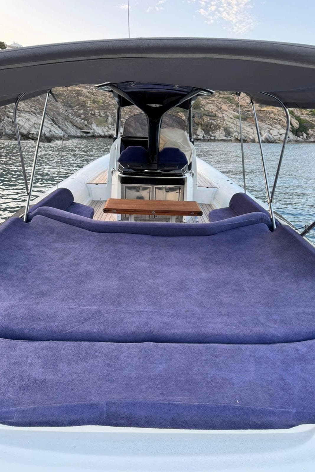2016 SACS Strider 13 yacht with spacious deck and purple seating, docked near rocky shoreline.