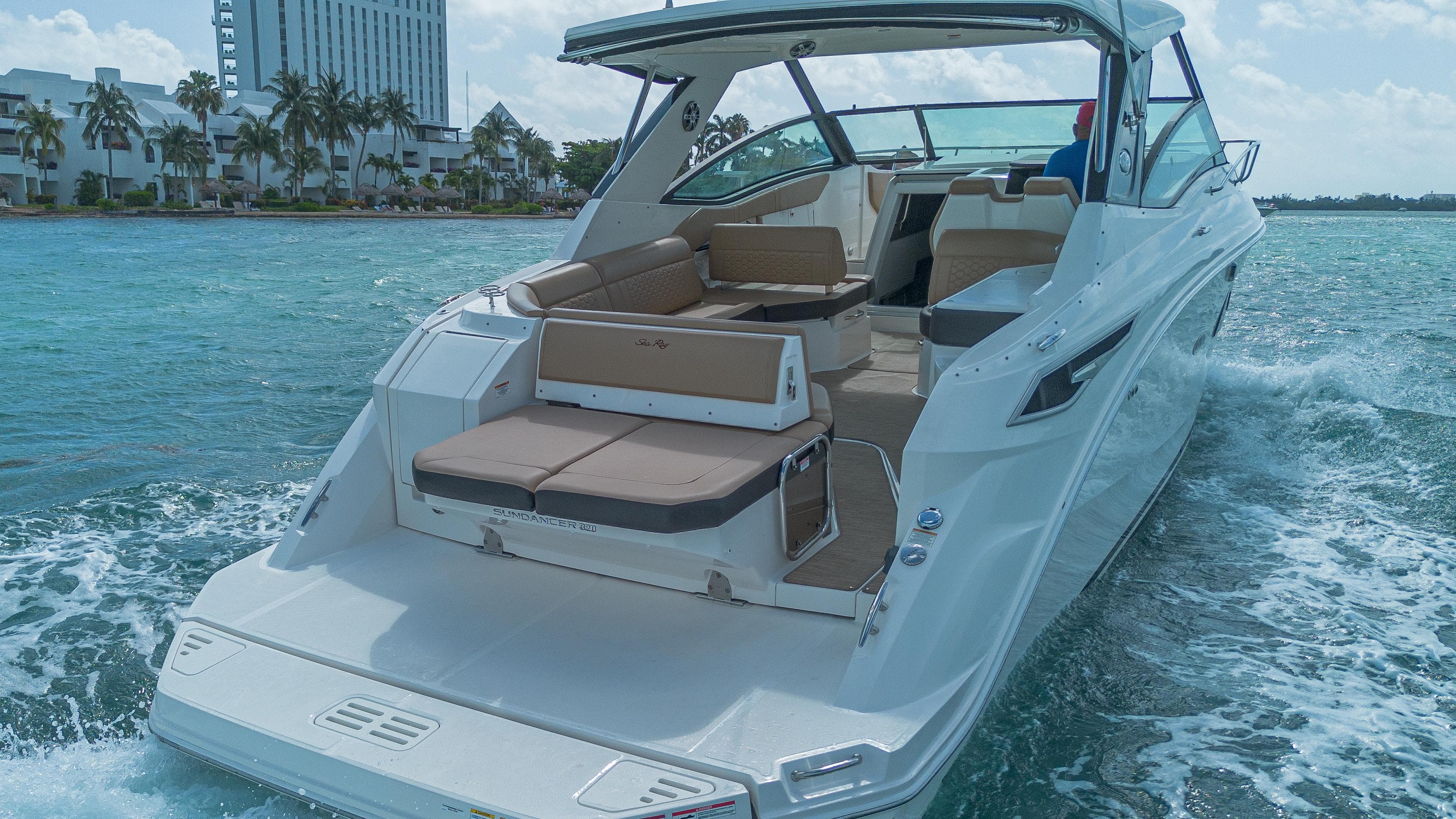 2023 Sea Ray Sundancer 320 cruising on clear blue water near a coastal city.