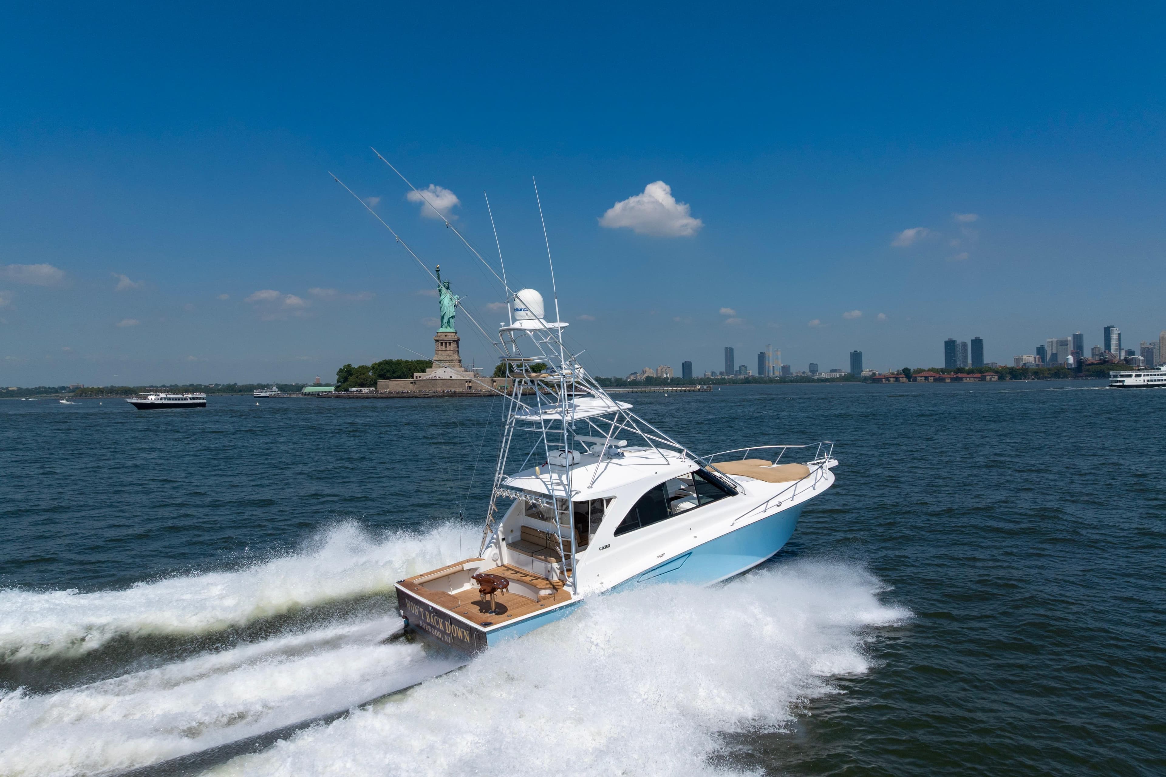 2012 Cabo 44 Hardtop Express yacht cruising near Statue of Liberty, clear blue sky.