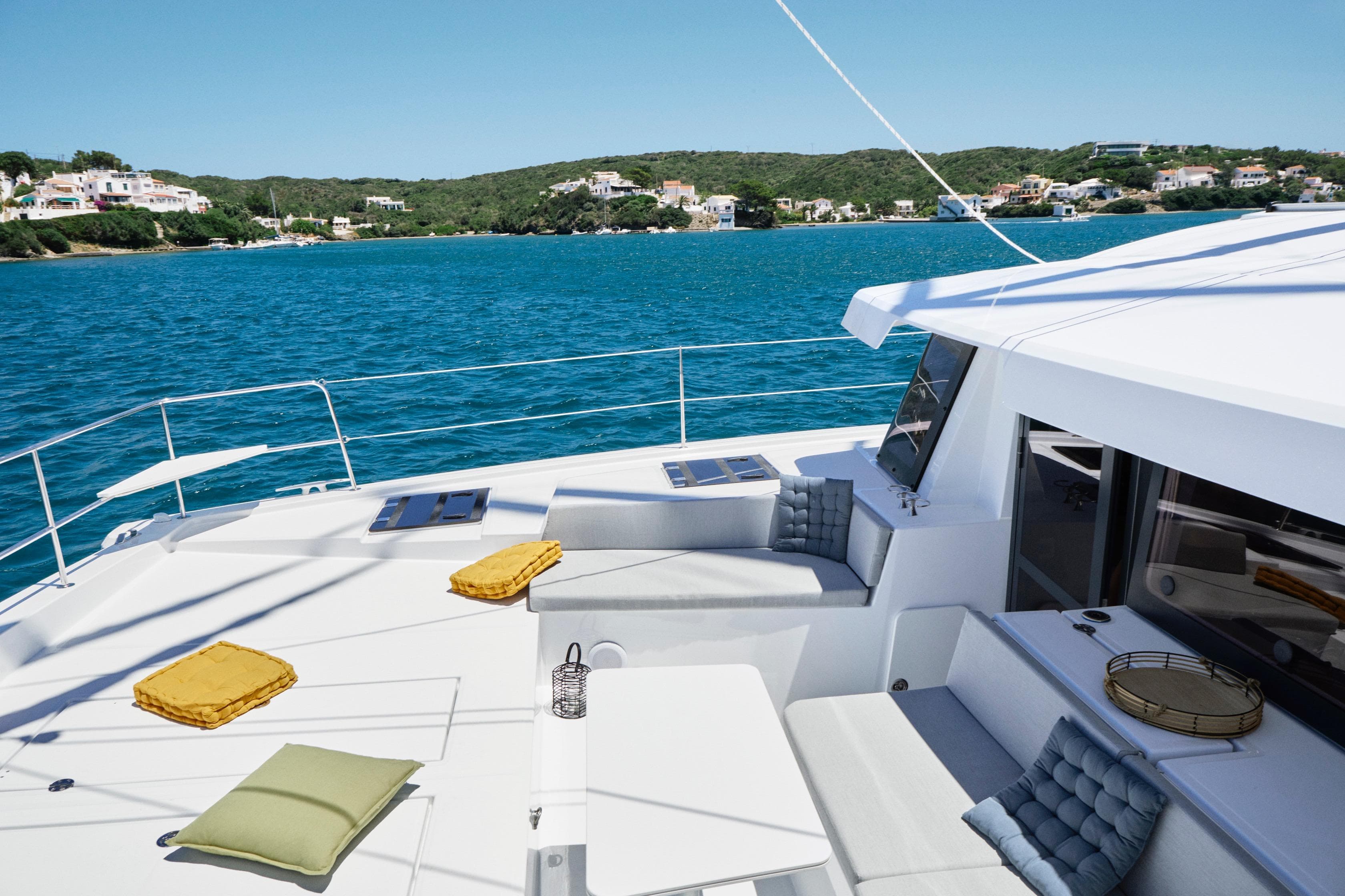 Luxurious Bali 4.4 yacht deck with cushions, overlooking serene blue waters and coastal homes.