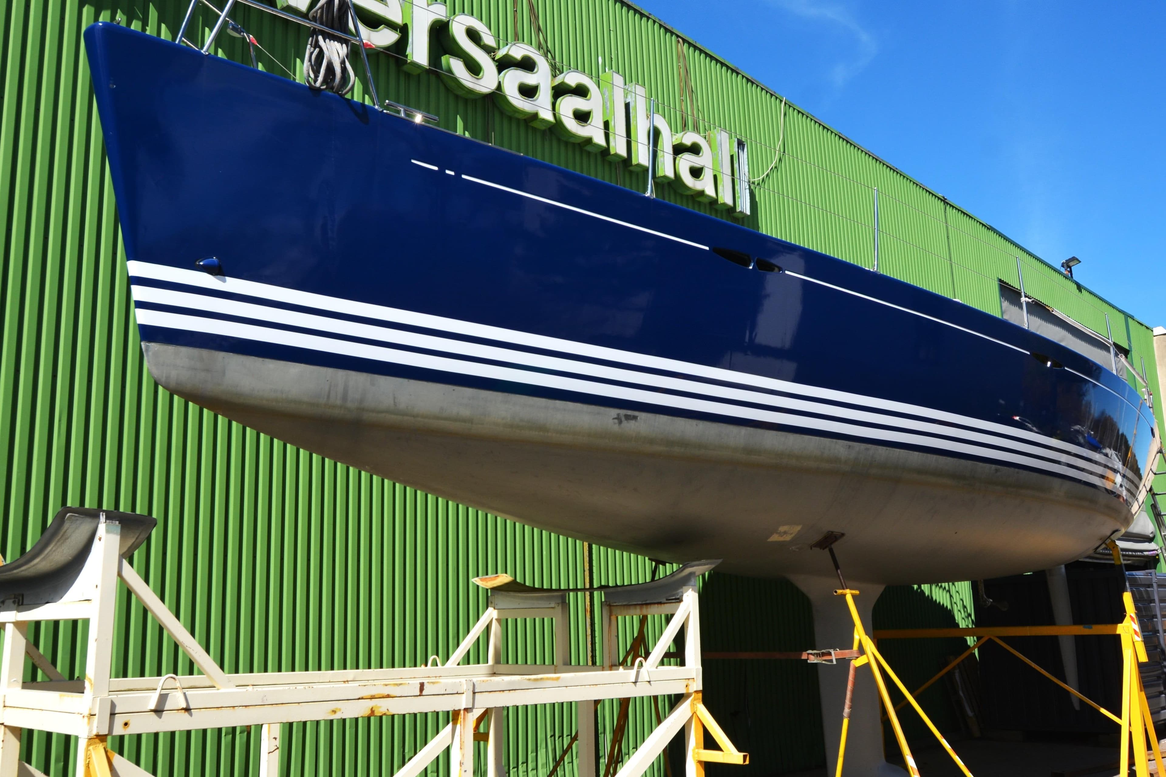 2004 X-Yachts X-46 sailboat in dry dock, blue hull with white stripes, green building background.