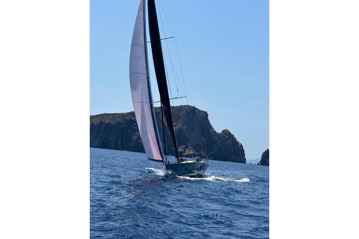 Sailing yacht Salona Ker 63 (2014) navigating near rocky coastline under clear blue sky.