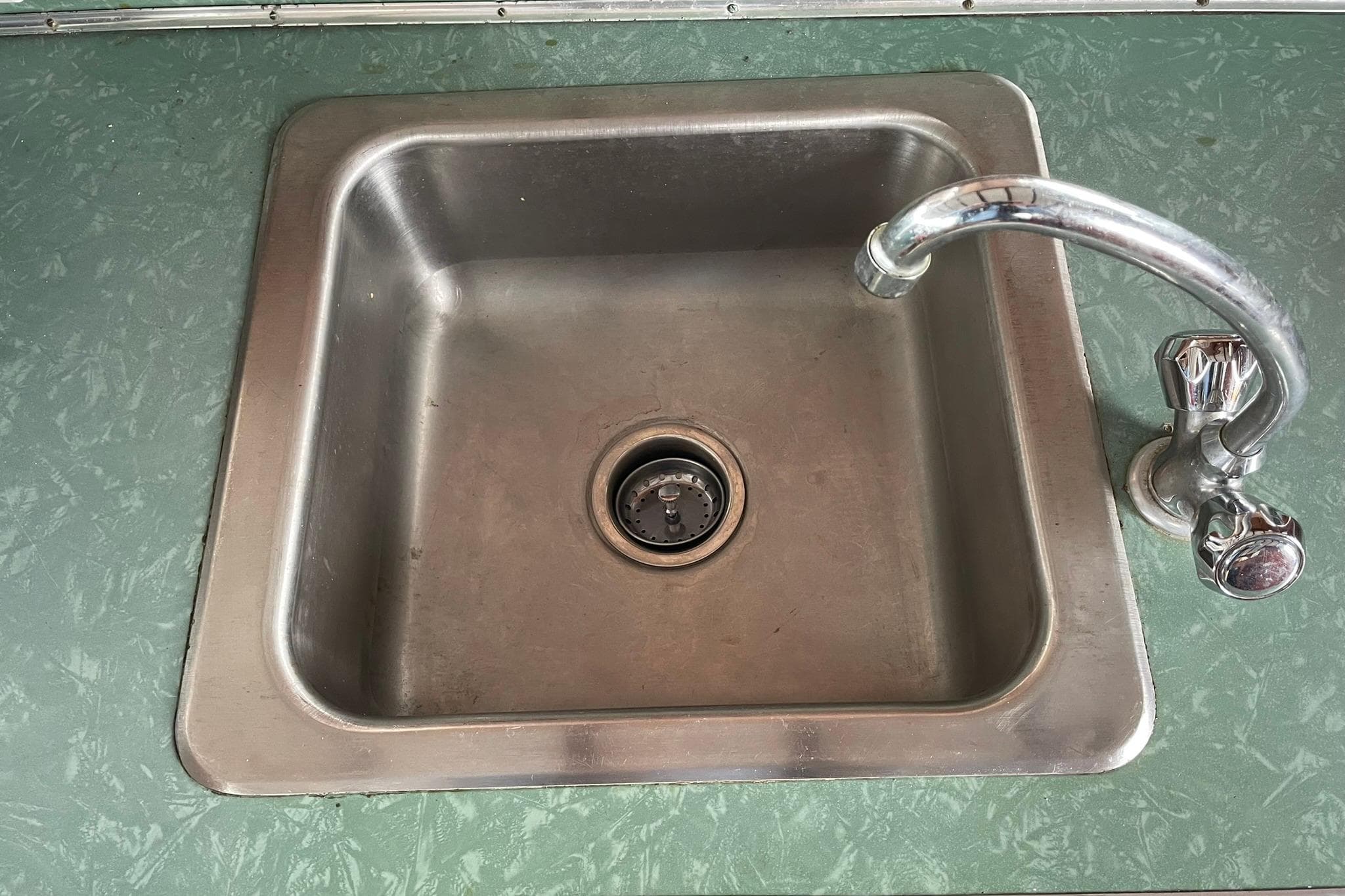Vintage 1948 Grandy 34 stainless steel sink with chrome faucet on green countertop.