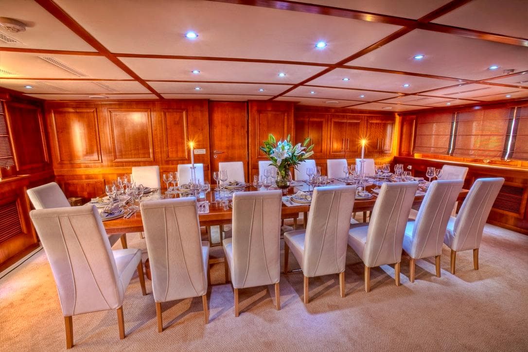 Luxurious yacht dining room with elegant table setting, white chairs, and wooden paneling, 1982 Husumer Shipyard.
