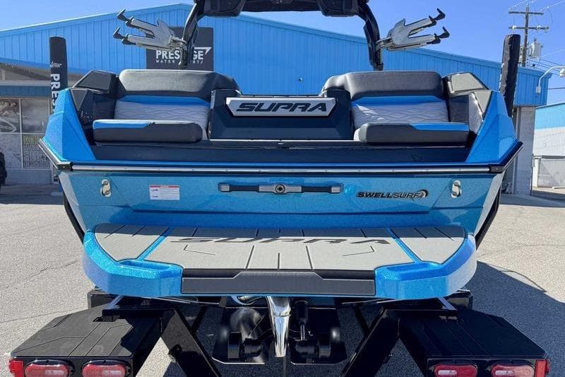 2026 Supra SL boat with blue exterior, featuring Swell Surf system, parked outdoors.