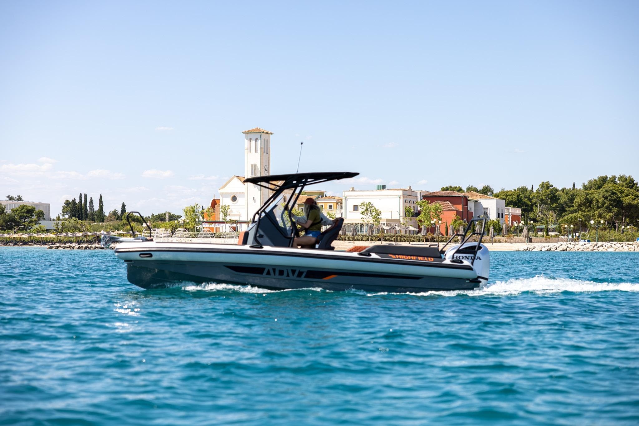 2026 Highfield ADV7 boat cruising on blue water near coastal buildings.