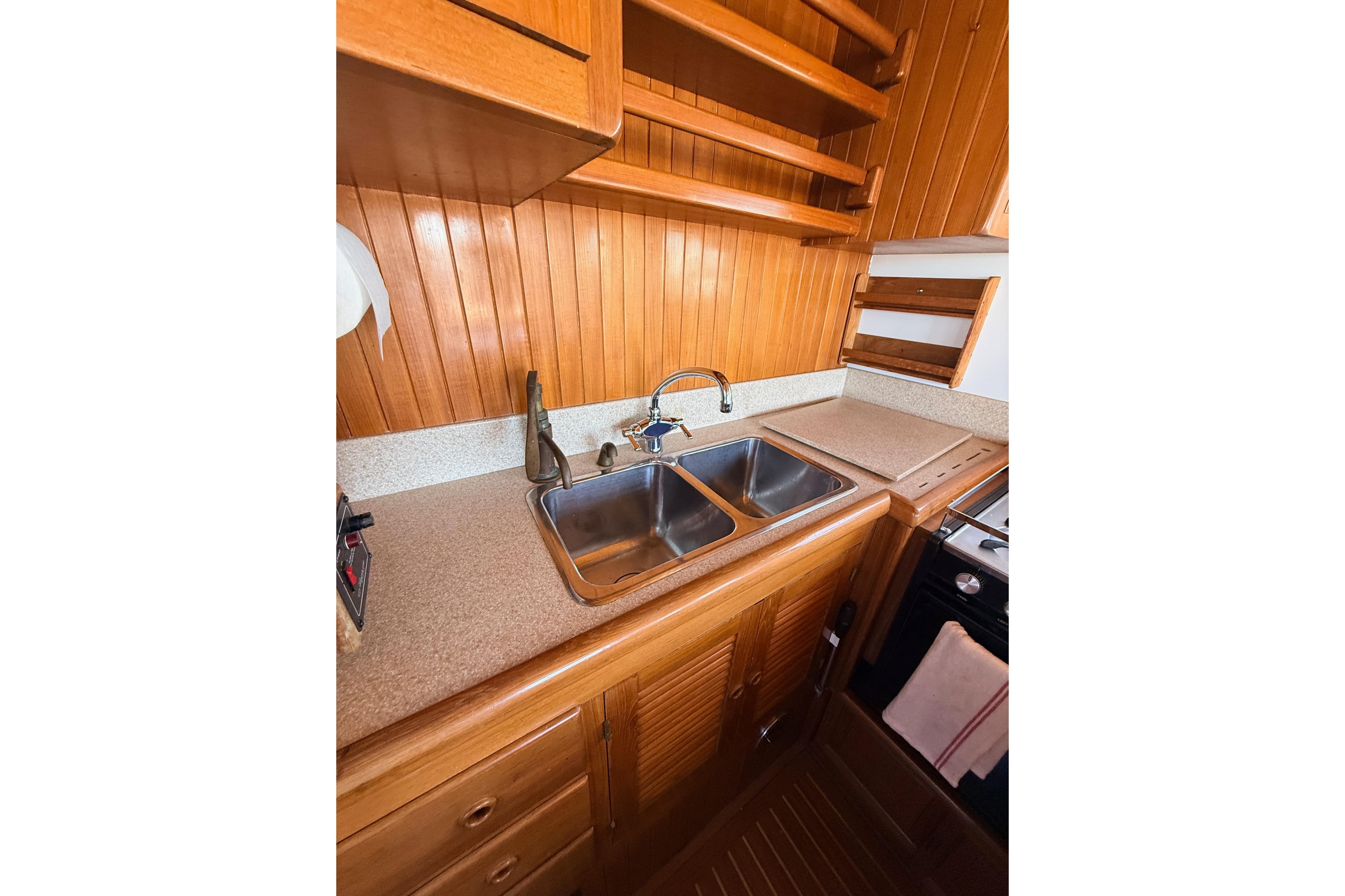 Wood-paneled kitchen in 1987 Lord Nelson Victory Tug, featuring double sink and shelving.