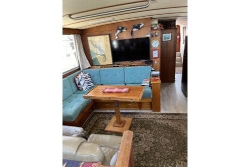 1983 Uniflite Cabin Cruiser interior with blue seating, wooden table, and wall-mounted TV.