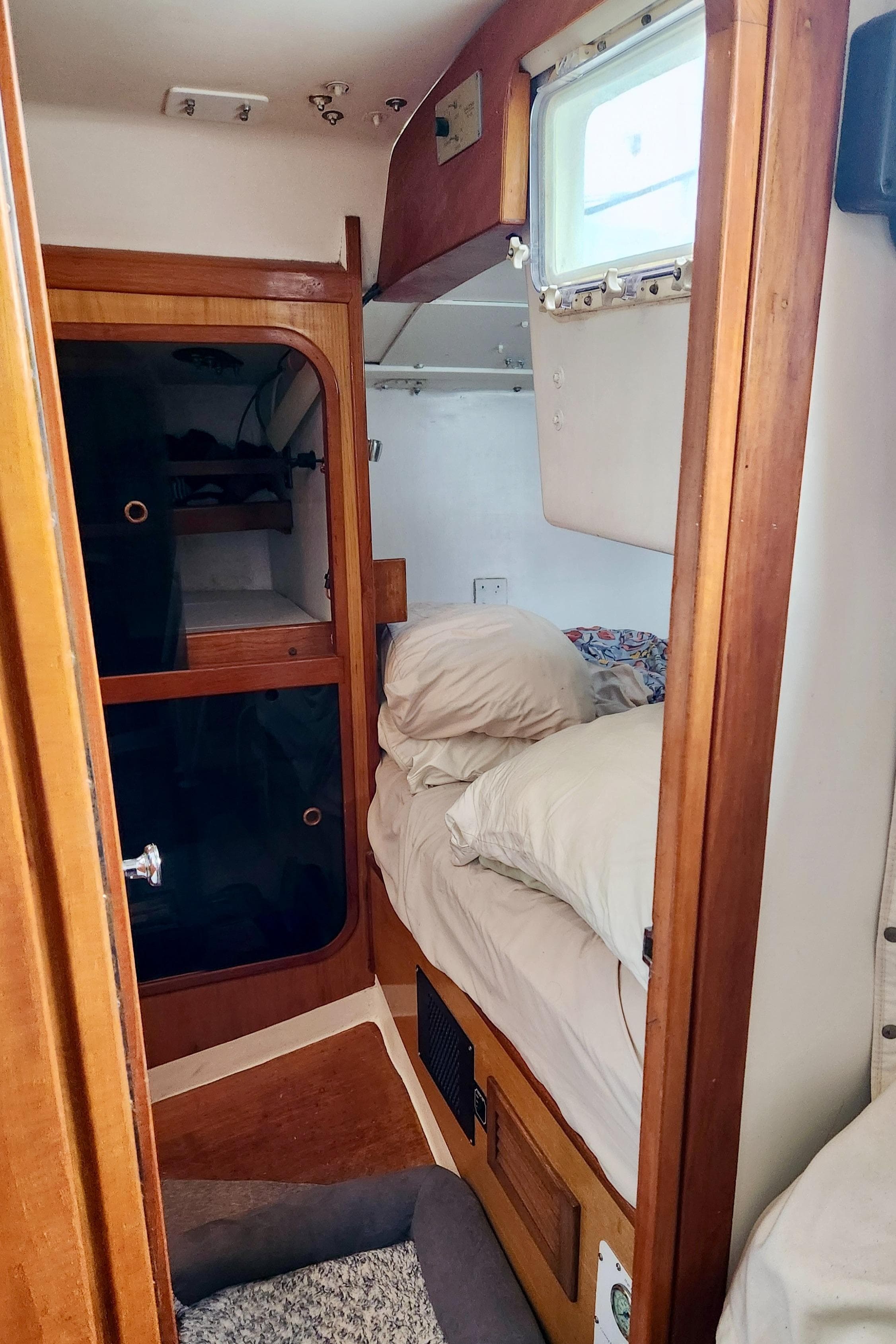Cozy cabin interior of a 1985 Farr 50 sailboat with wooden furnishings and bedding.