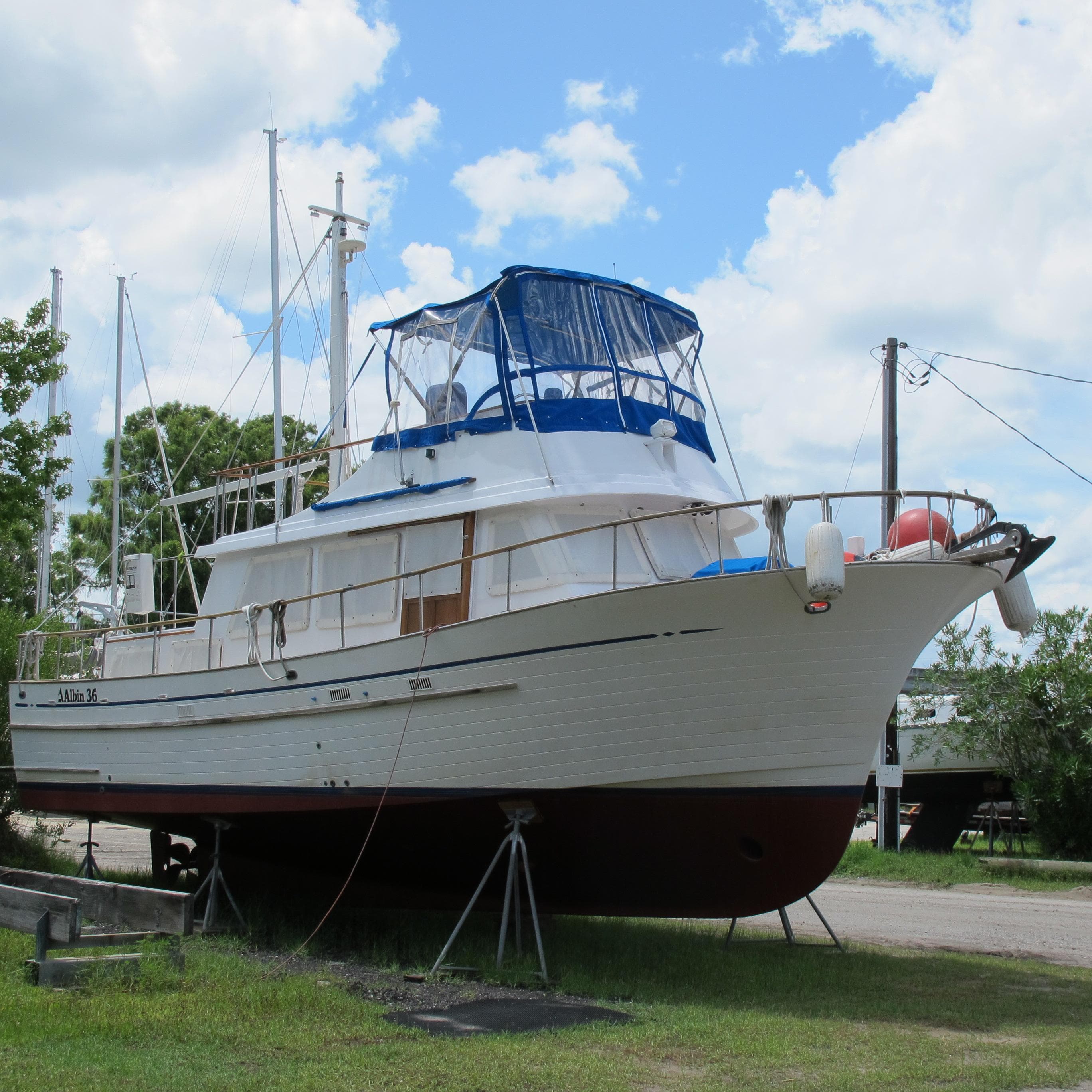 1981 Albin 36 boat on land with blue canopy under a cloudy sky.