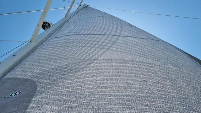 Sail of 2023 Jeanneau 65 yacht against clear blue sky.