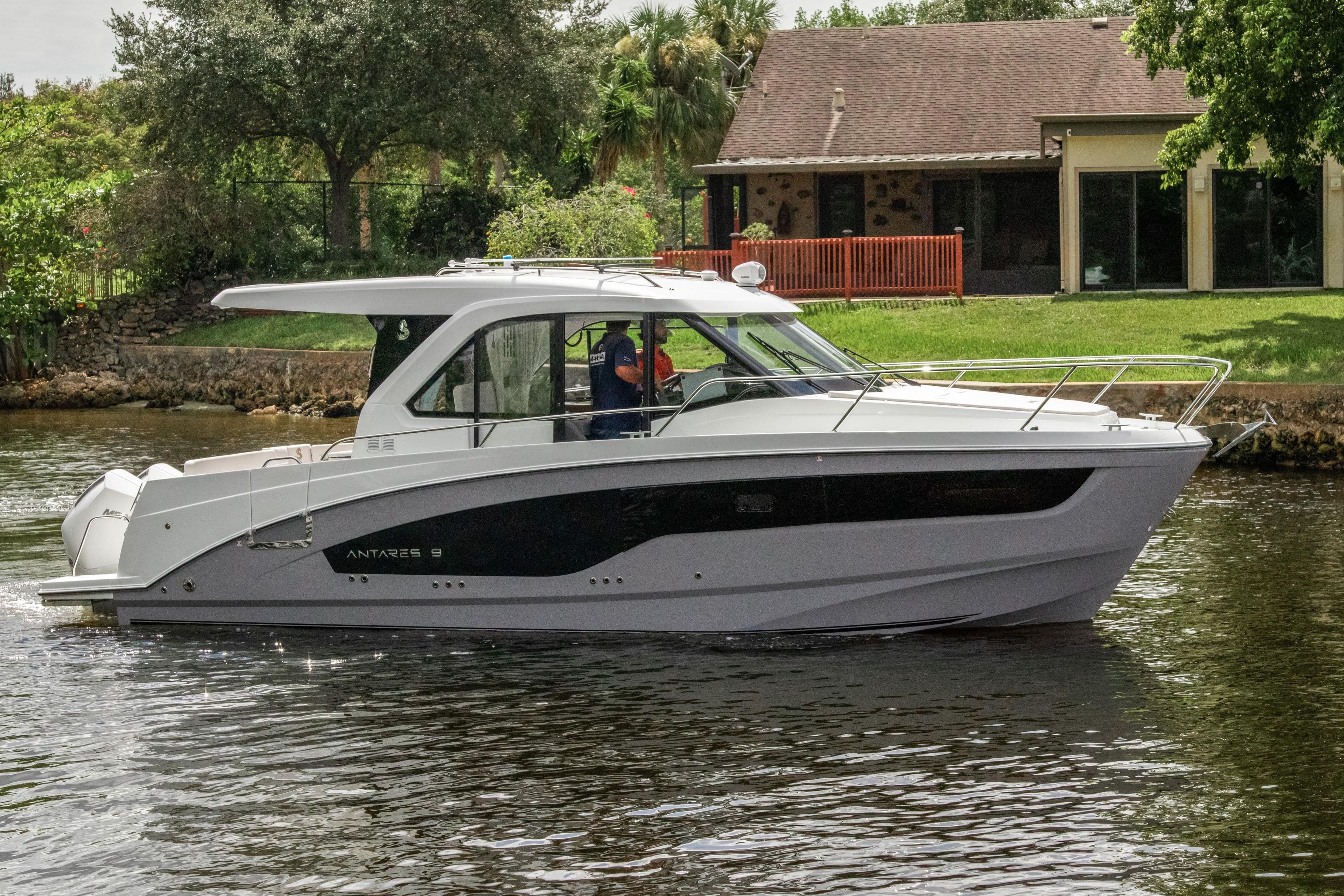 2026 Beneteau Antares 9 boat cruising on a calm river near a house.