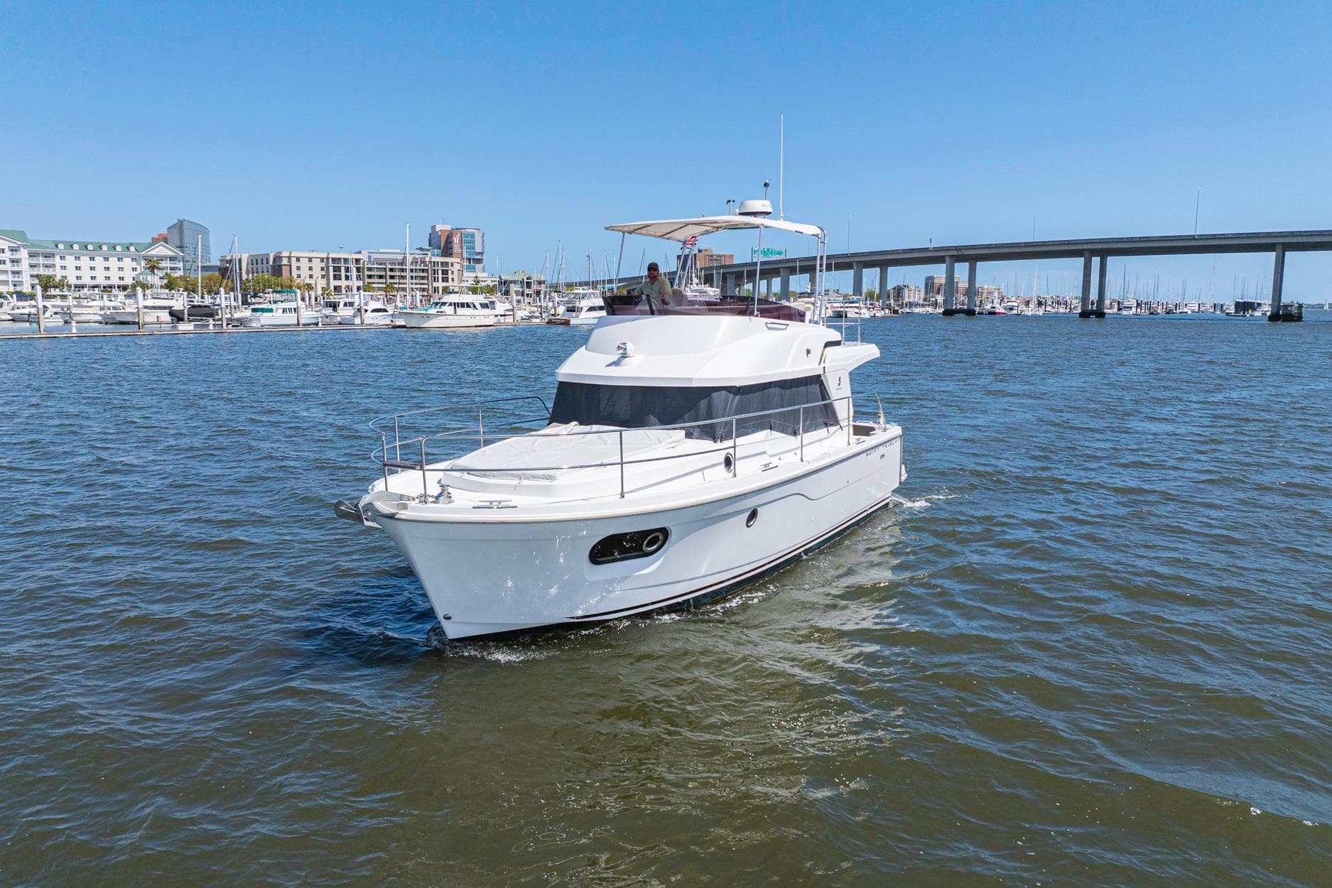 2019 Beneteau Swift Trawler 35 cruising in a marina with cityscape and bridge backdrop.