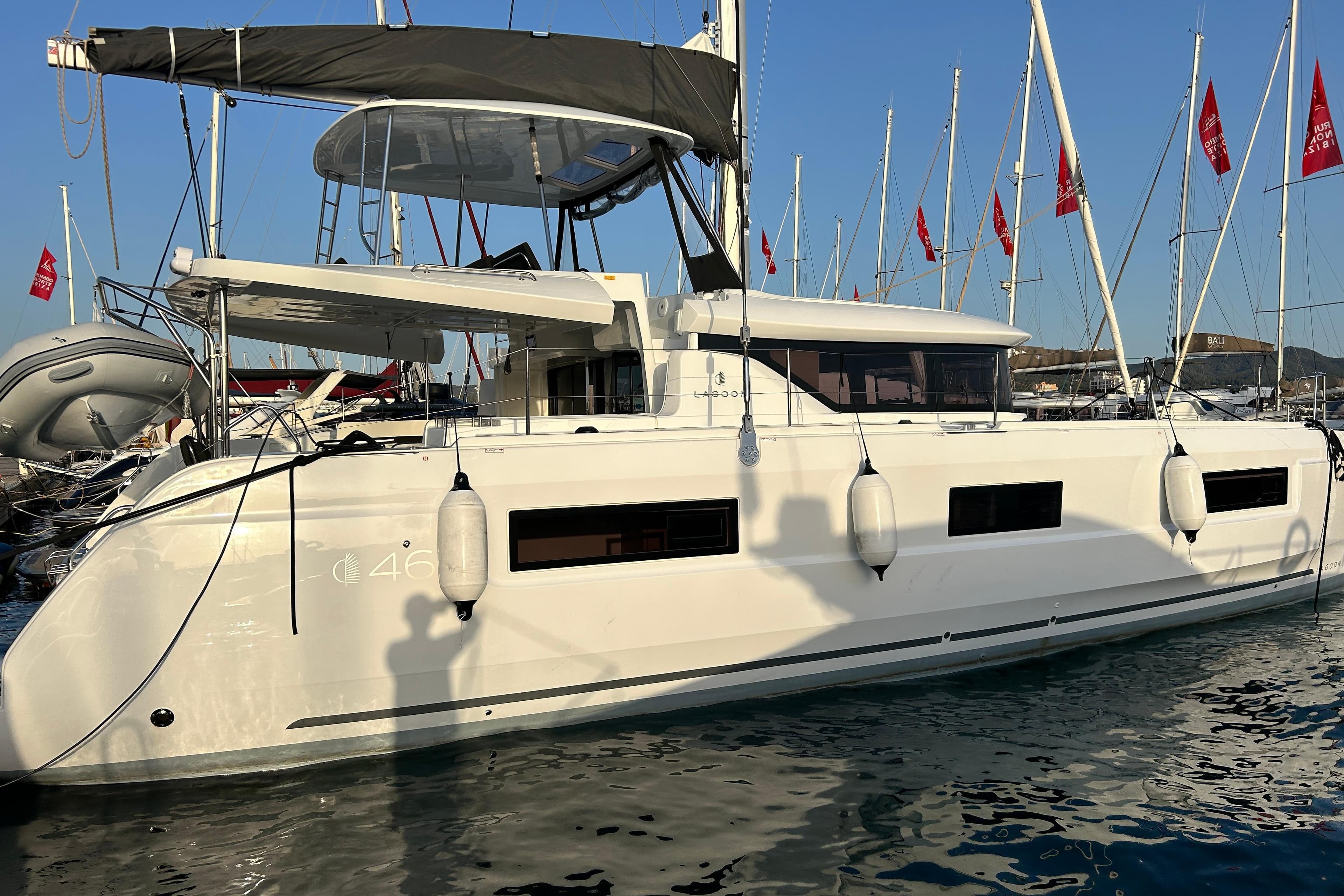2024 Lagoon 46 catamaran docked at marina with red flags in background.