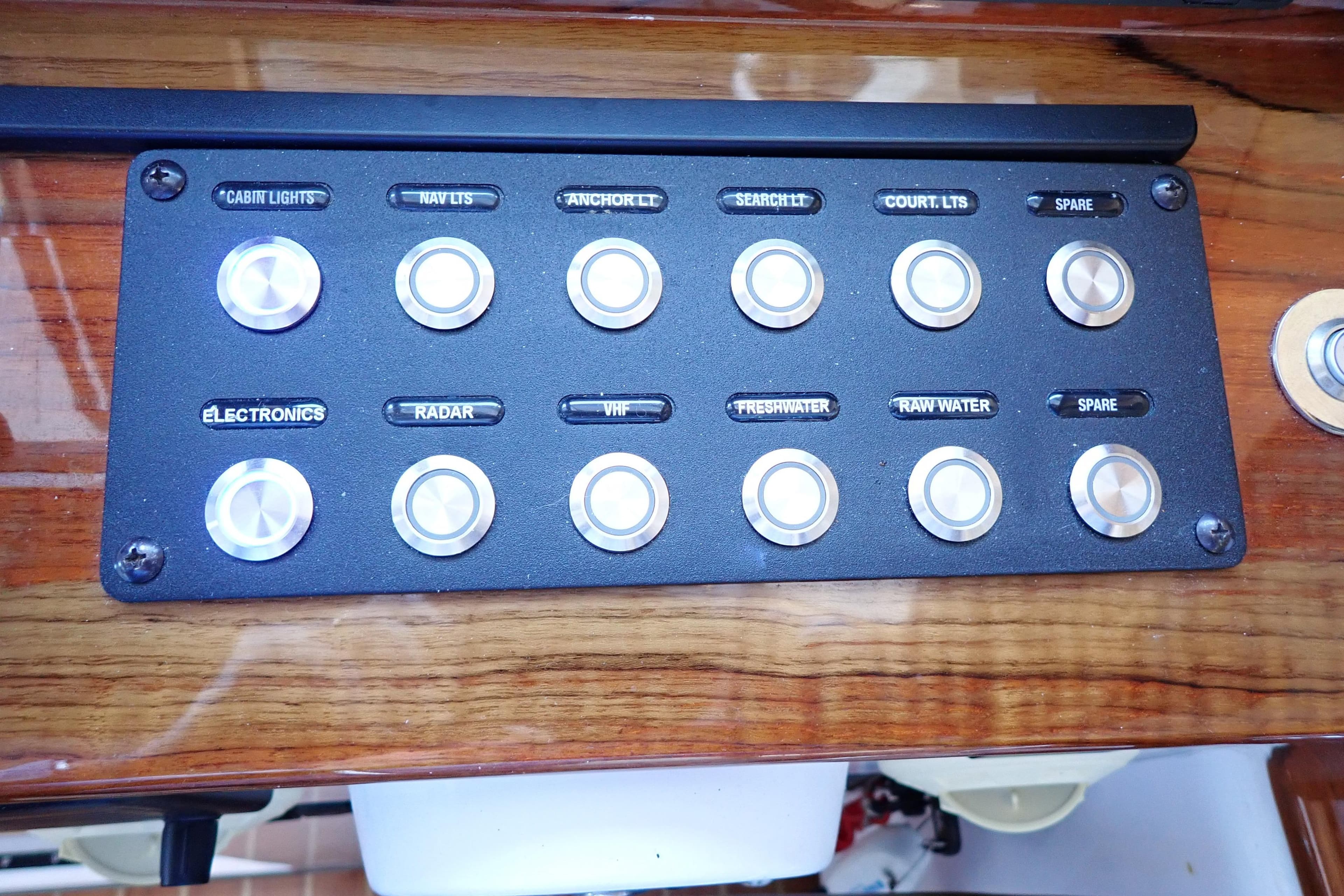 Control panel of 2023 True North 34 Outboard Express with labeled switches on wood finish.