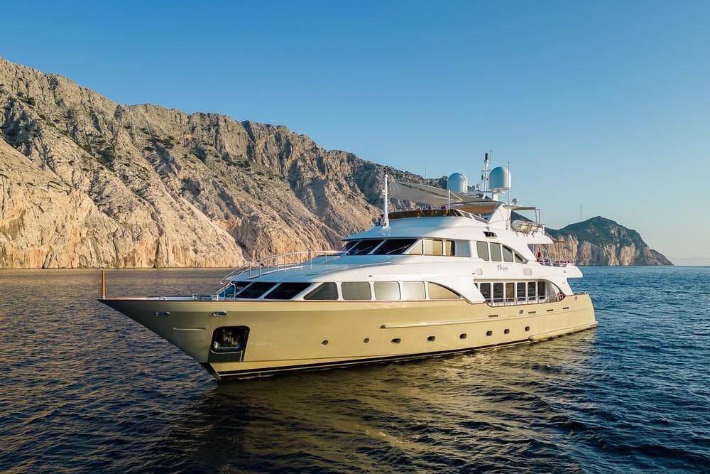 Luxurious 2008 Benetti Classic 120 yacht cruising near rocky coastline at sunset.