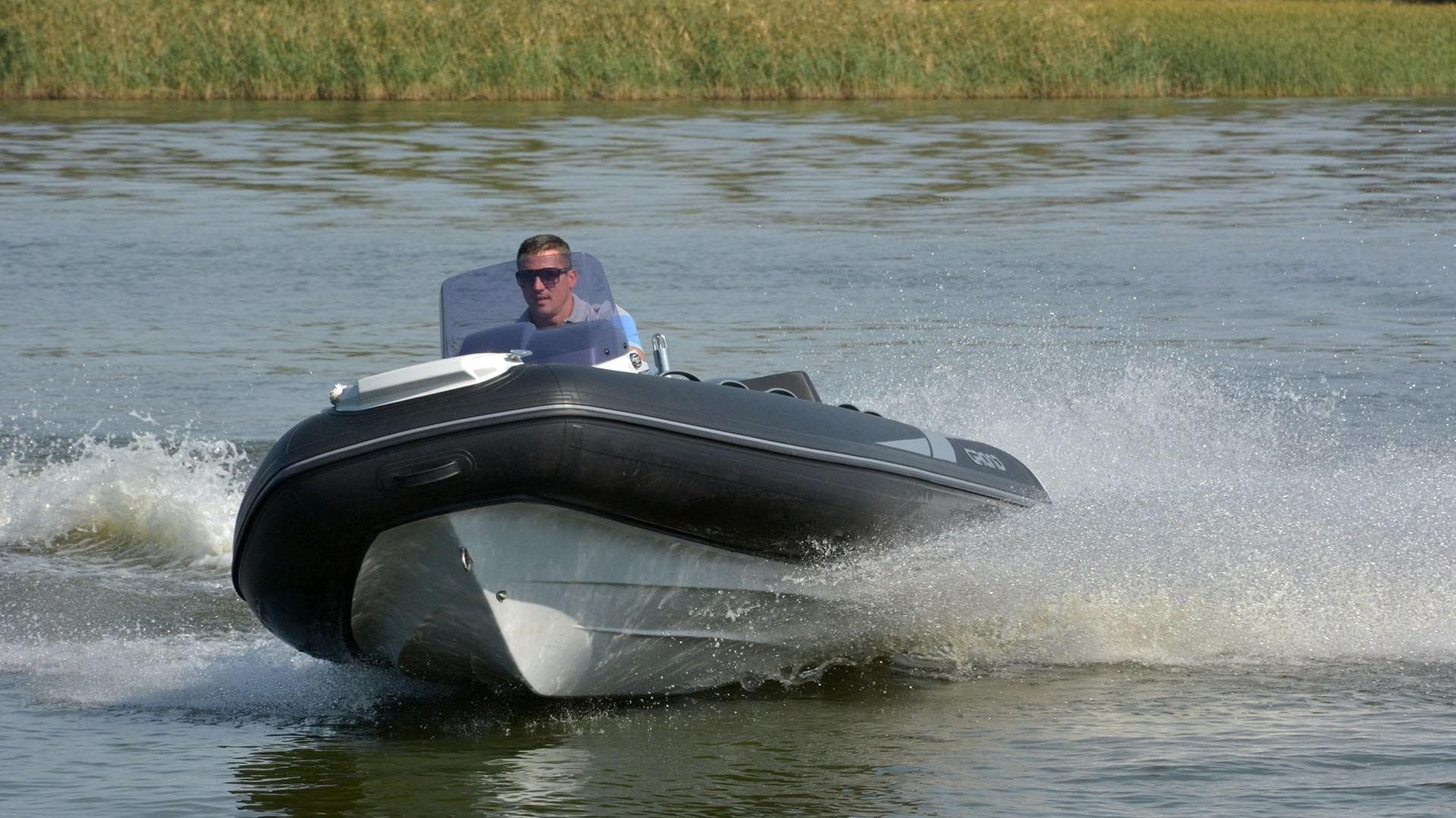 2025 Grand Inflatables G420 boat speeding on water with driver, creating splashes.
